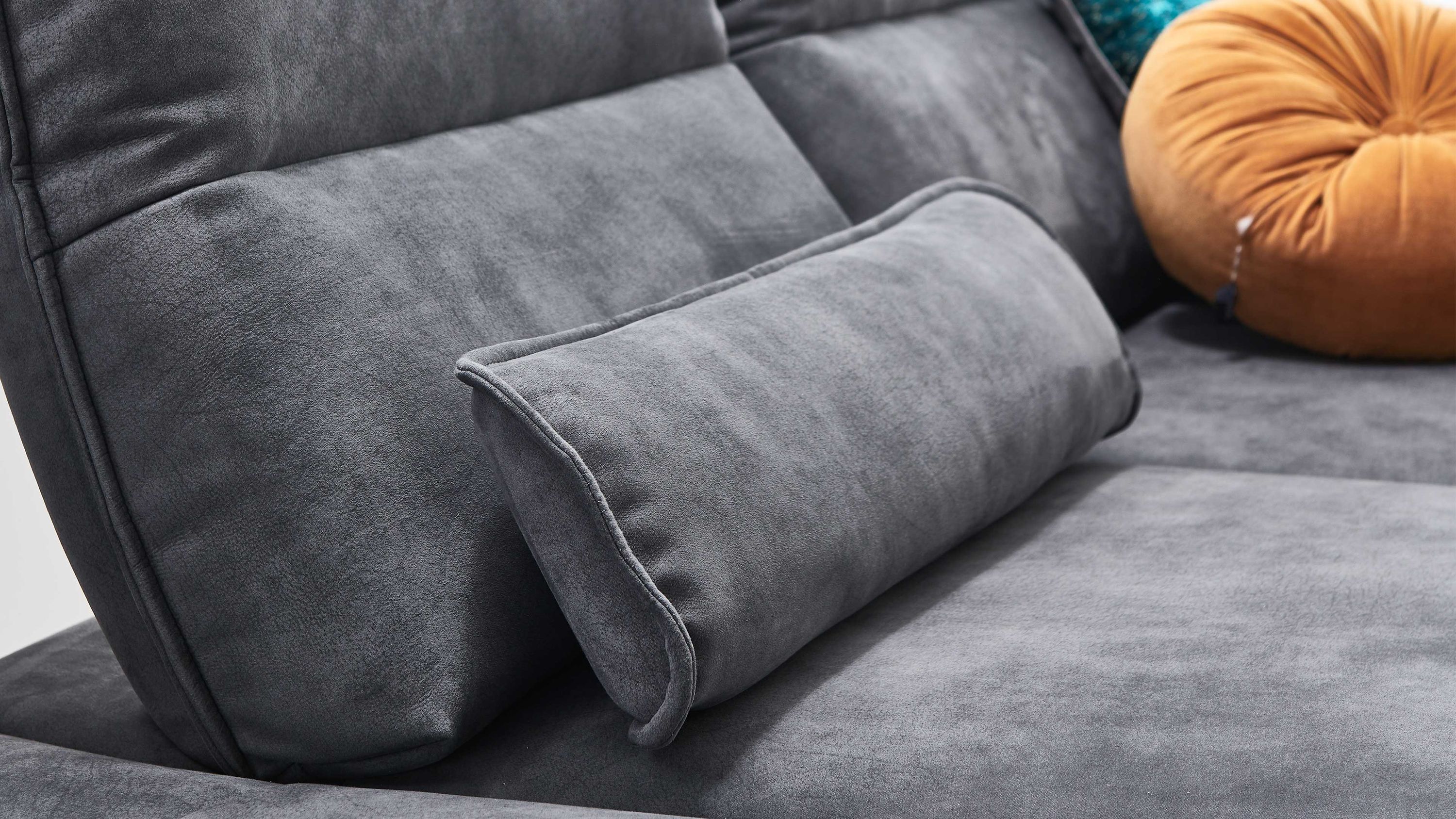 Rechteckiges Nierenkissen in grauem Bezug auf grauem Polstersofa mit rundem orangen Kissen im Hintergrund