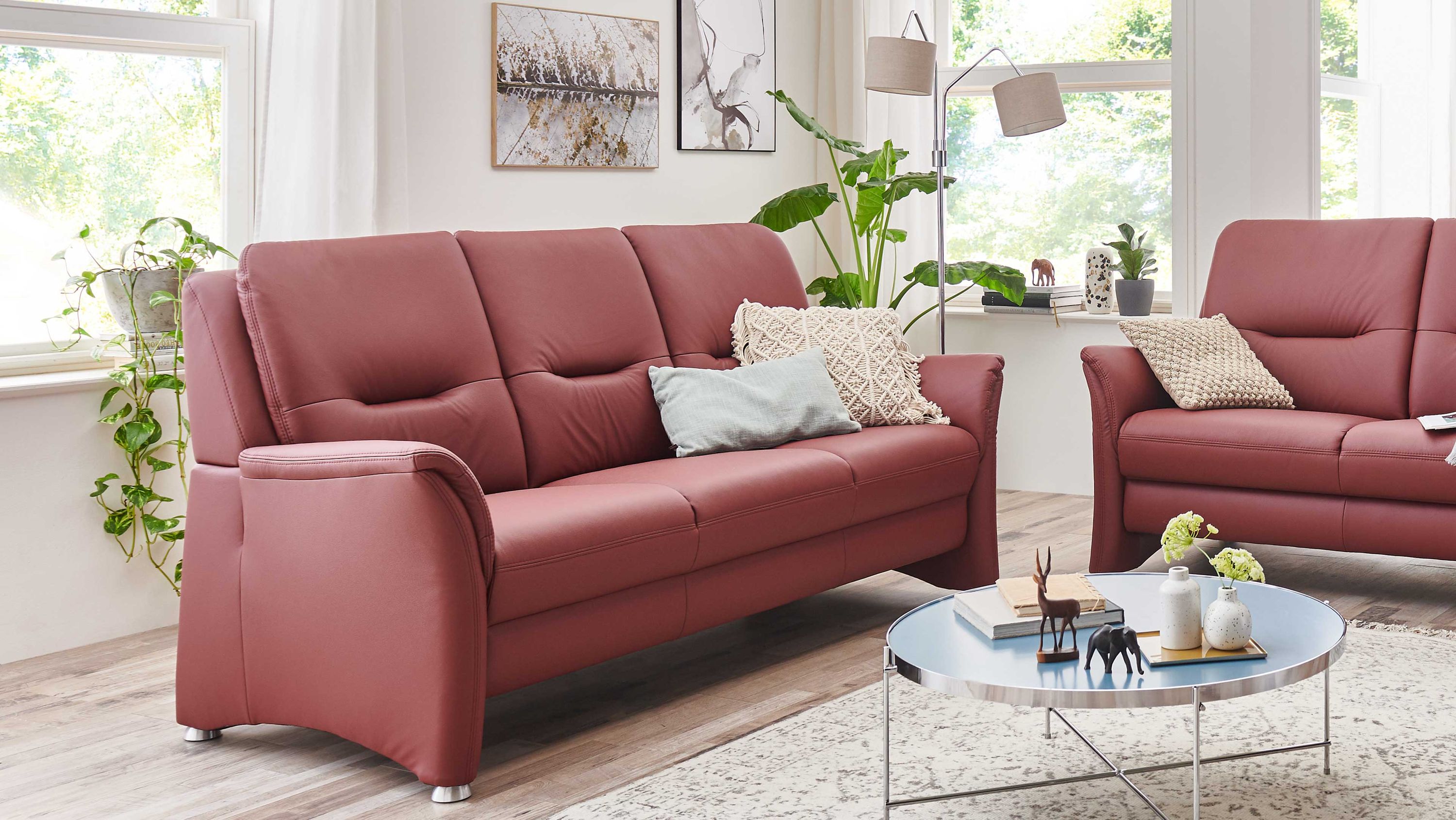 Dreisitziges brombeerfarbenes Sofa mit Metallfüßen Dreisitziges Sofa in brombeerfarbener Polsterung mit Metallfüßen in hellem Wohnzimmer