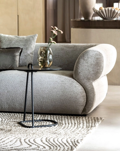 Sofa mit modernem Beistelltisch und Blumenvase. Graues Sofa mit geschwungener Armlehne, schwarzer Beistelltisch mit Vase und Blume auf gemustertem Teppich.