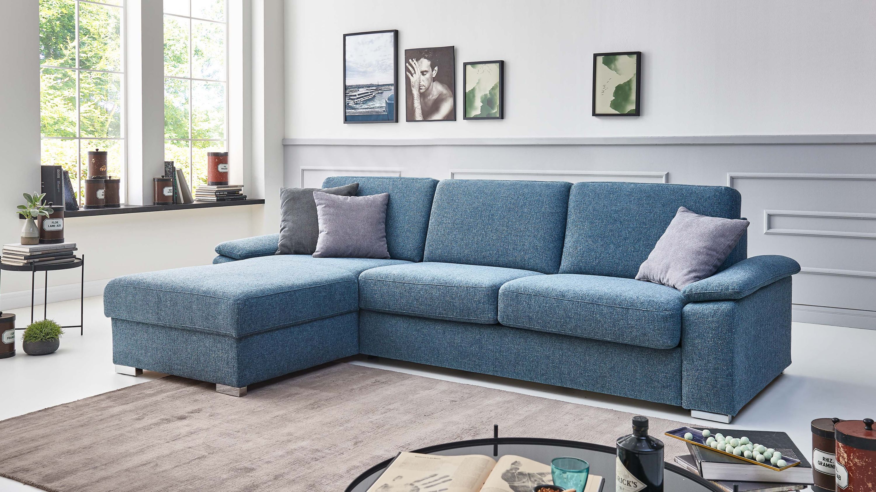 Ecksofa mit türkisfarbenem Stoffbezug drei Sitzkissen zwei graue Zierkissen und Chromfüßen in modernem Wohnzimmer
