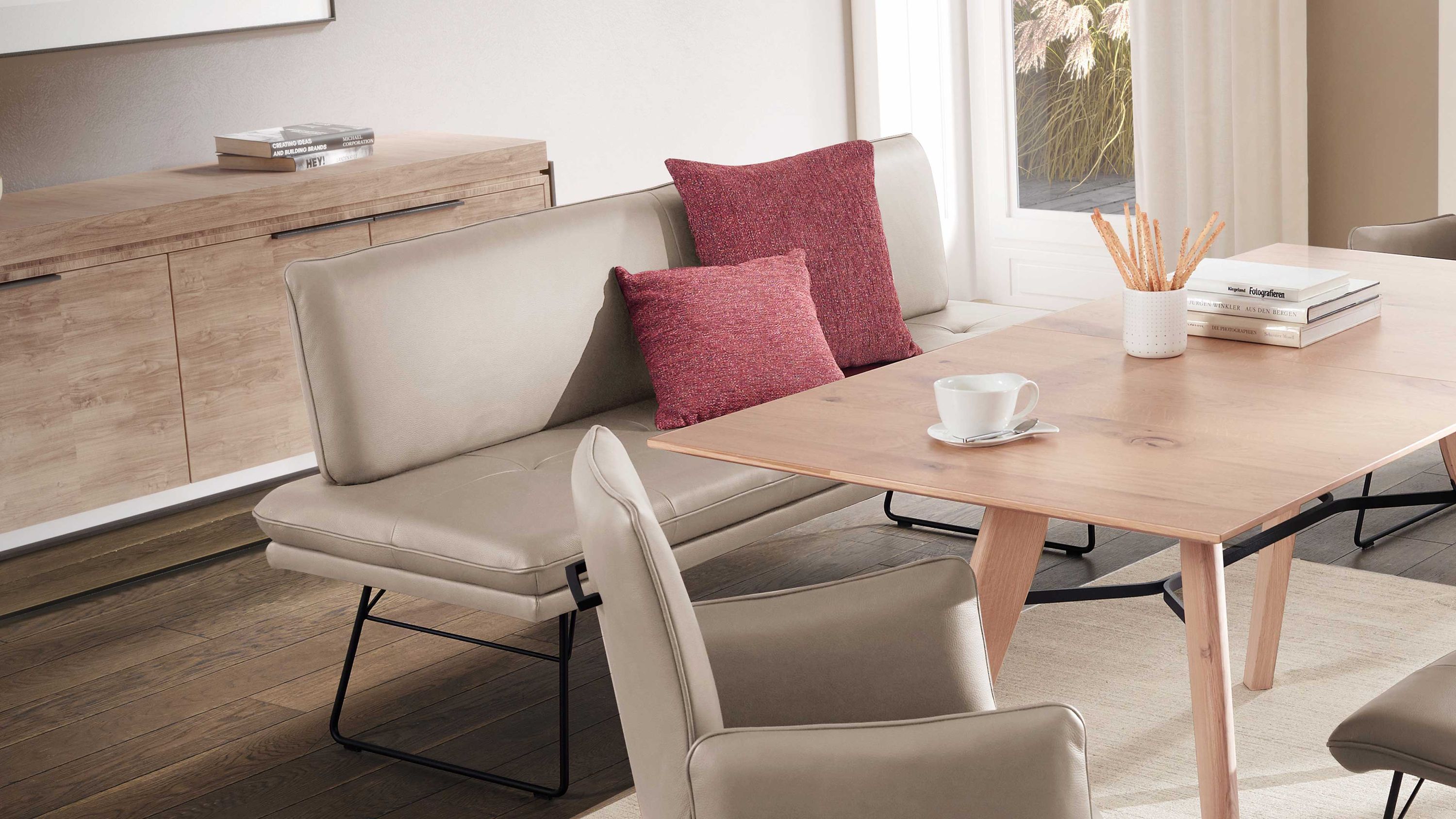 Hellgraue Polsterbank mit Rückenlehne und schwarzem Kufengestell in einem Esszimmer mit Holztisch