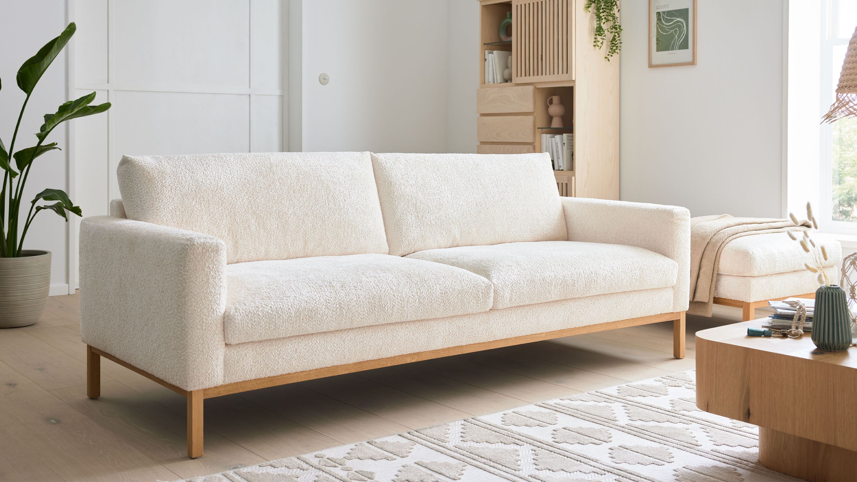 Dreisitzer Sofa mit weißem Stoffbezug und Holzfüßen Dreisitziges Sofa mit weißem Stoffbezug und Holzfüßen in hellem Wohnzimmer