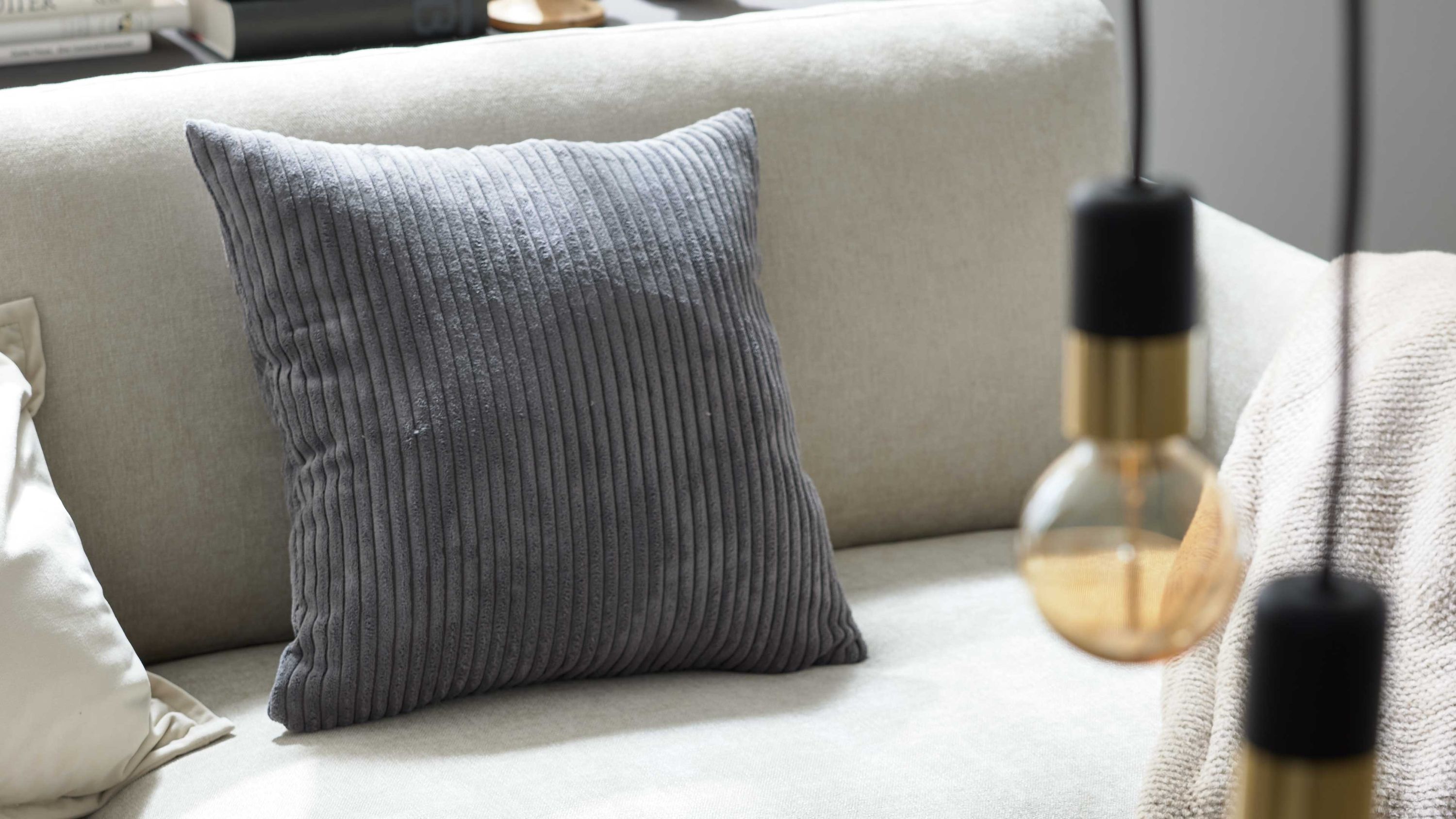 Quadratische Kissenhülle aus breitem Cordstoff in aschegrau auf einem hellen Sofa