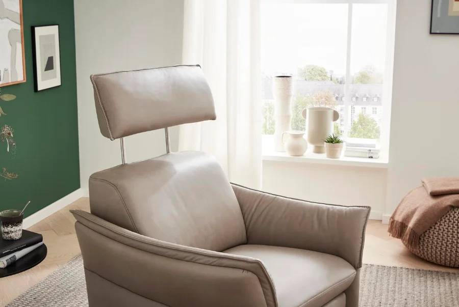 Moderner beige-grauer Ledersessel mit verstellbarer Kopfstütze in hell eingerichtetem Wohnzimmer mit Grünwand und Fensternische.