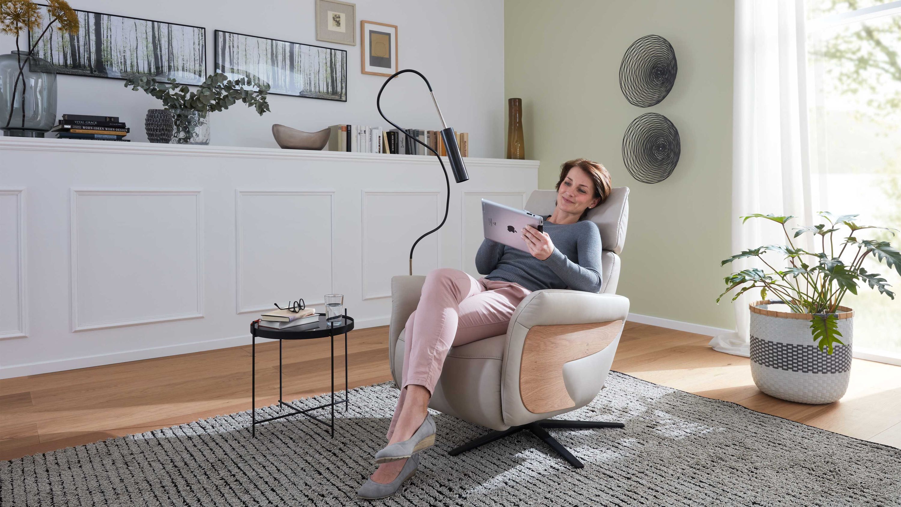 Relaxsessel mit klifffarbenem Bezug und anthrazitfarbenem Sternfuß in modernem Wohnzimmer mit Frau auf Tablet