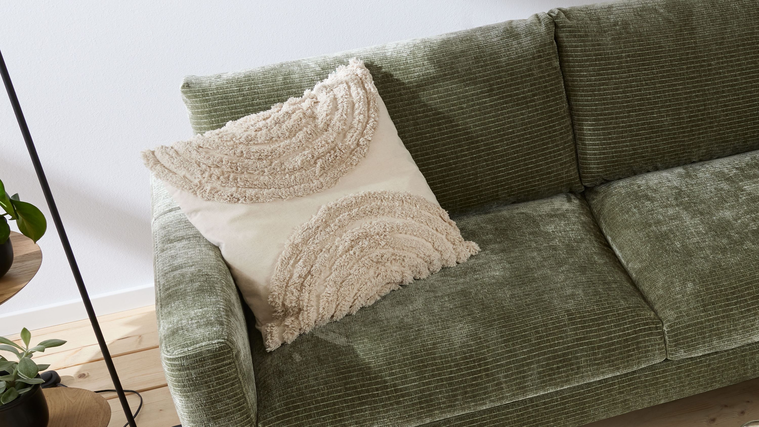 Beige Kissenhülle mit halbkreisförmigen strukturierten Mustern auf grünem Sofa