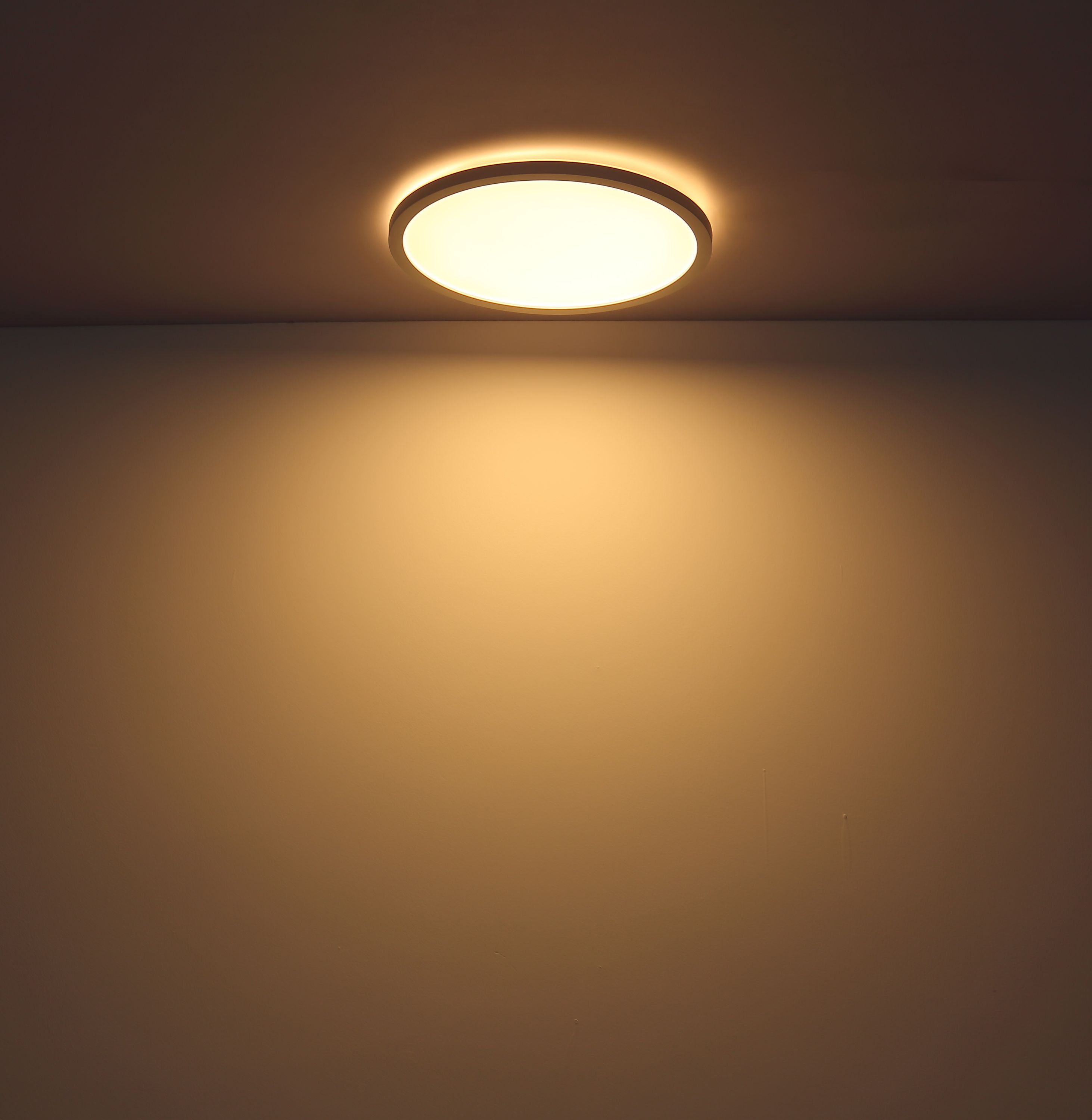 Eingeschaltete, runde Deckenleuchte flach an der Decke montiert, strahlt warmes Licht aus