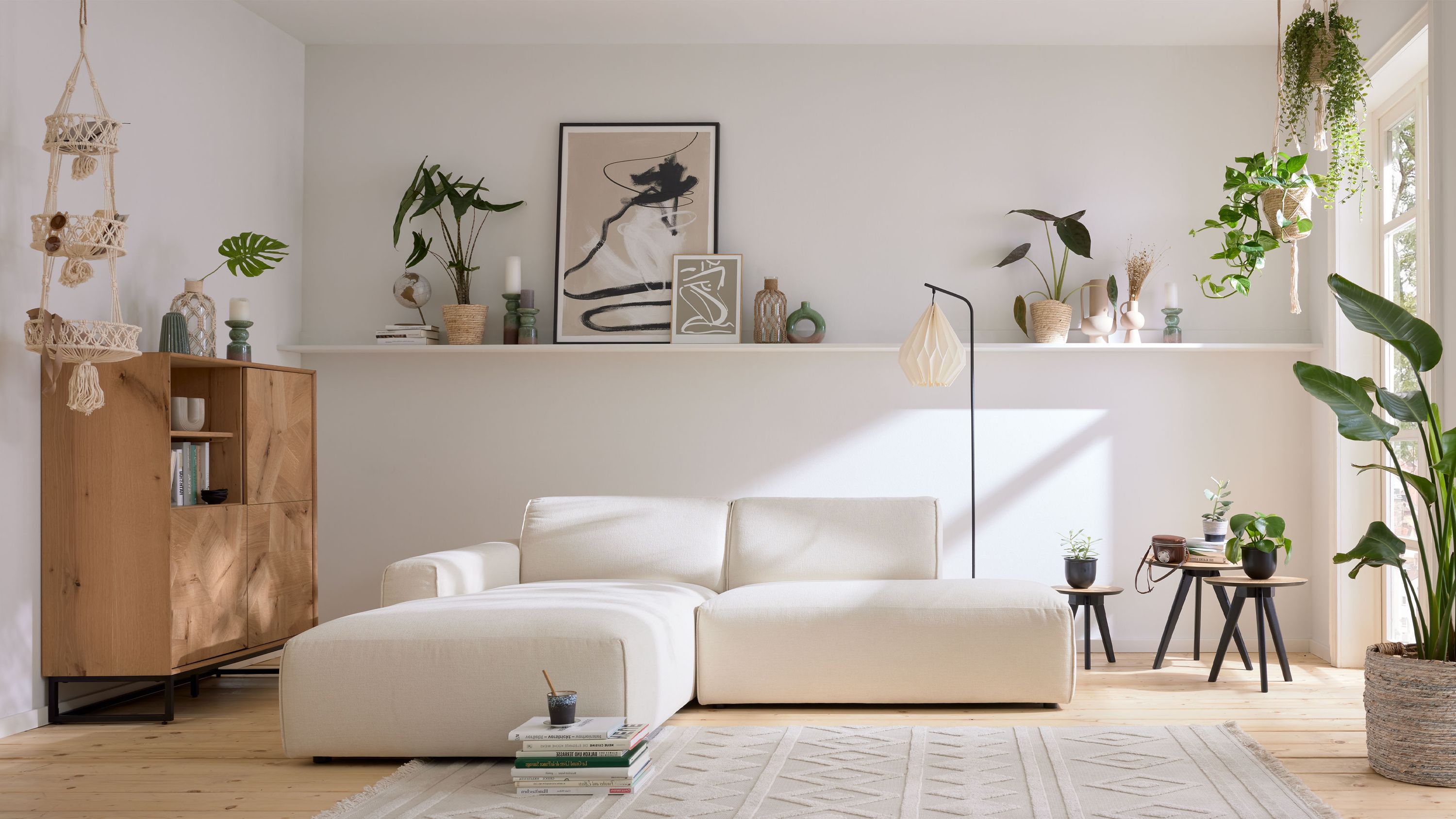 Ecksofa in weiß mit linksseitiger Ottomane in einem hellen Wohnzimmer mit Holzboden und Pflanzen