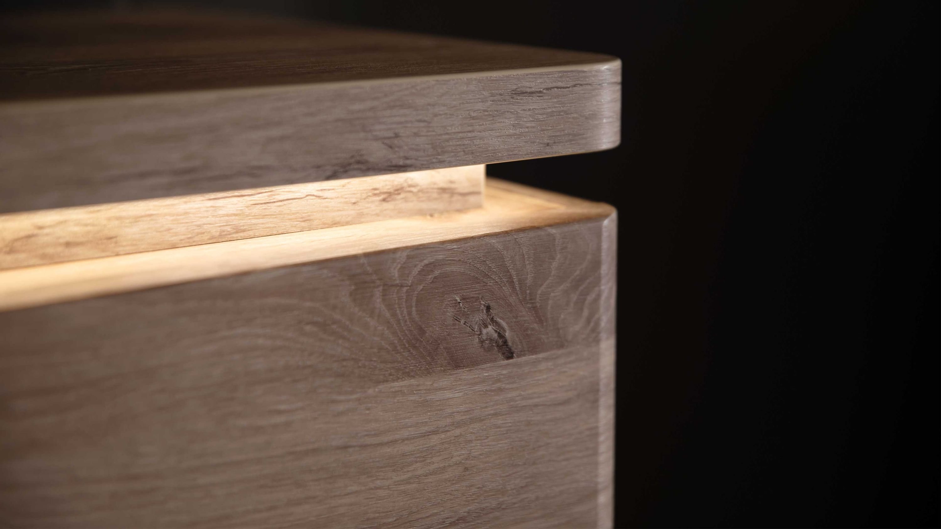 Nahaufnahme eines Holzmöbelstücks mit integrierter LED-Bandbeleuchtung unter der oberen Ablage