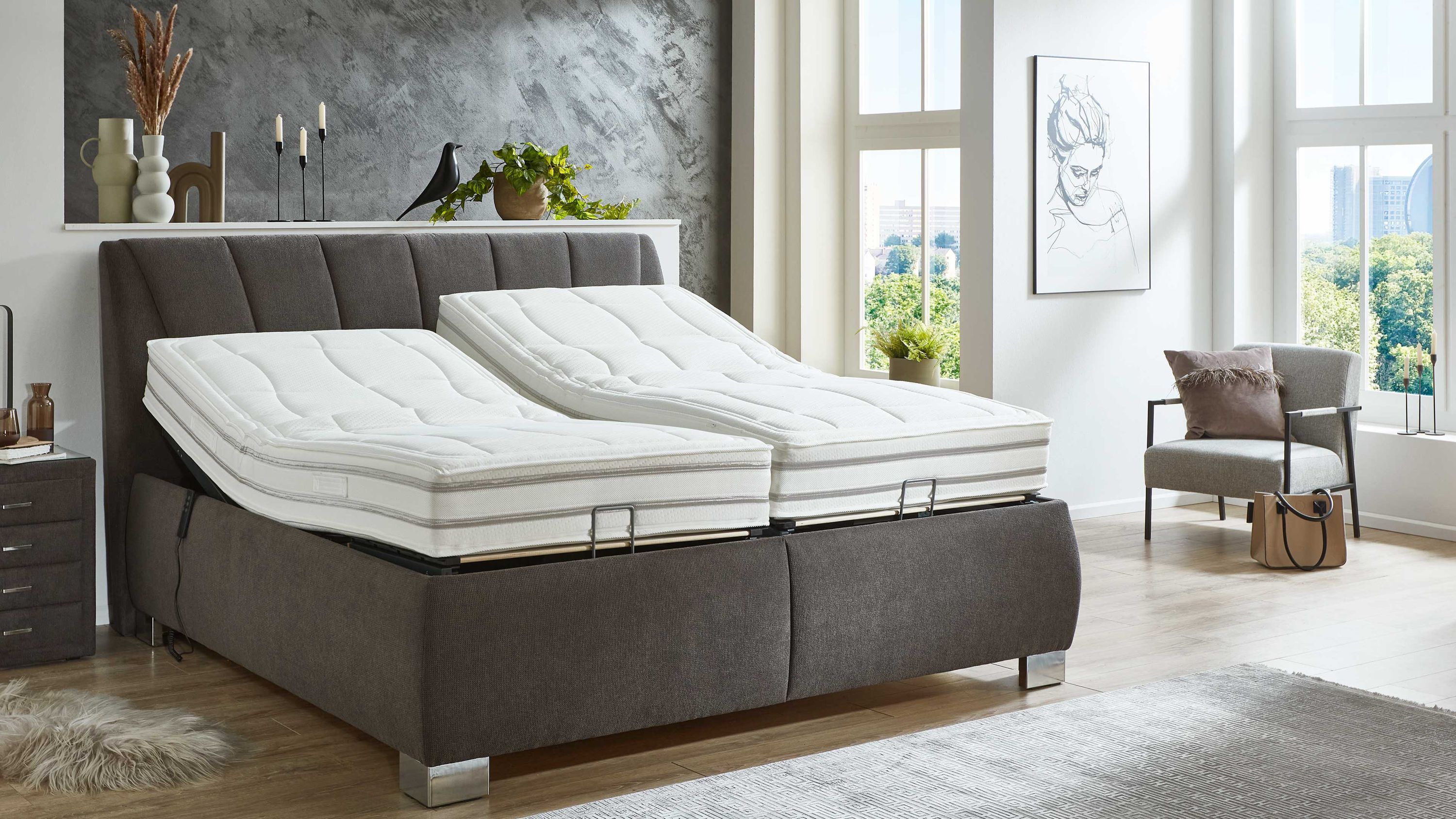 Boxspringbett mit anthrazitfarbenem Stoffbezug und motorisch verstellbaren Lattenrahmen in hellem Schlafzimmer