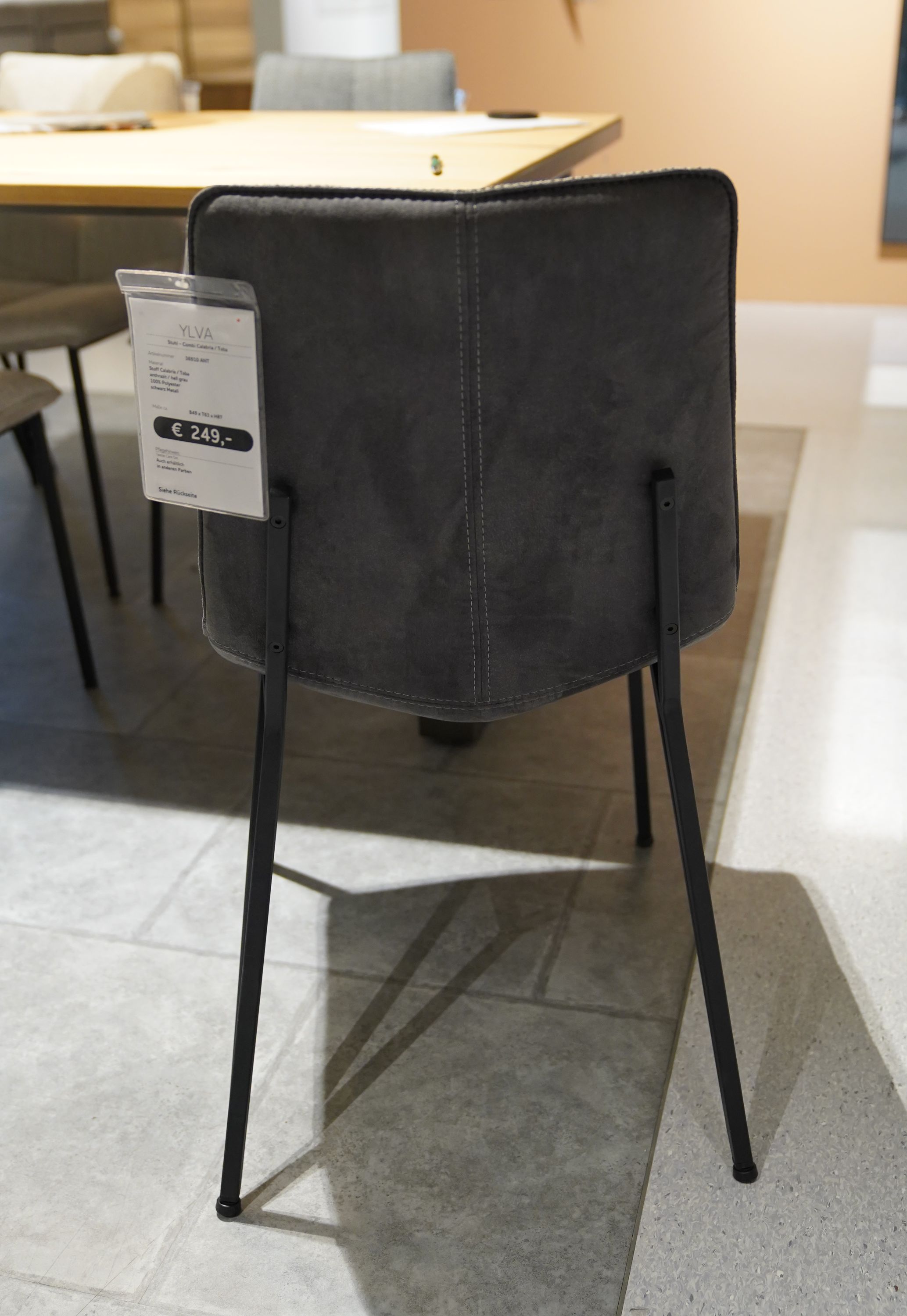 Stuhl mit dunkelgrauem Bezug und schwarzem Metallgestell von hinten vor einem Esstisch fotografiert