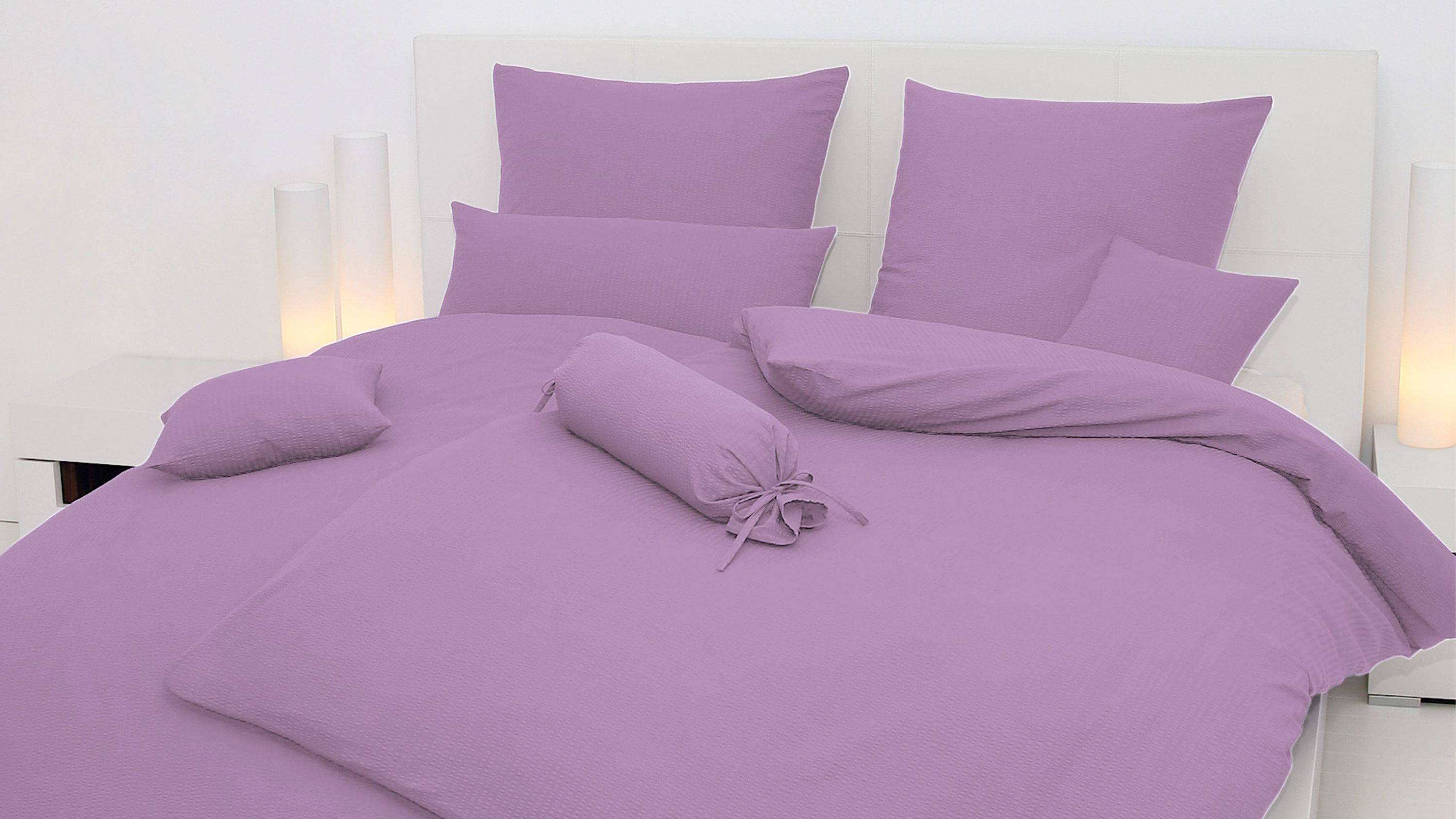 Doppelbett mit fliederfarbener Bettwäsche bestehend aus Kissen Zierkissen und Bettdecke