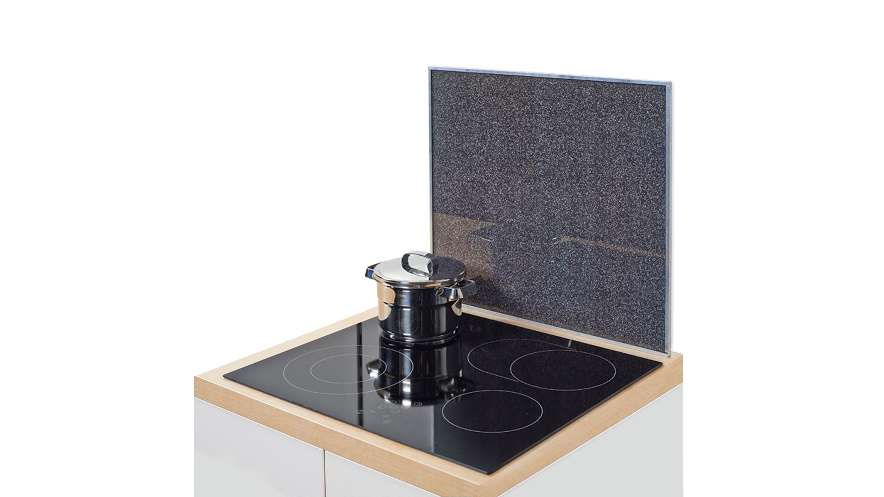 Anthrazitfarbene Rückwand aus Glas mit Granitoptik hinter einem schwarzen Kochfeld mit Topf