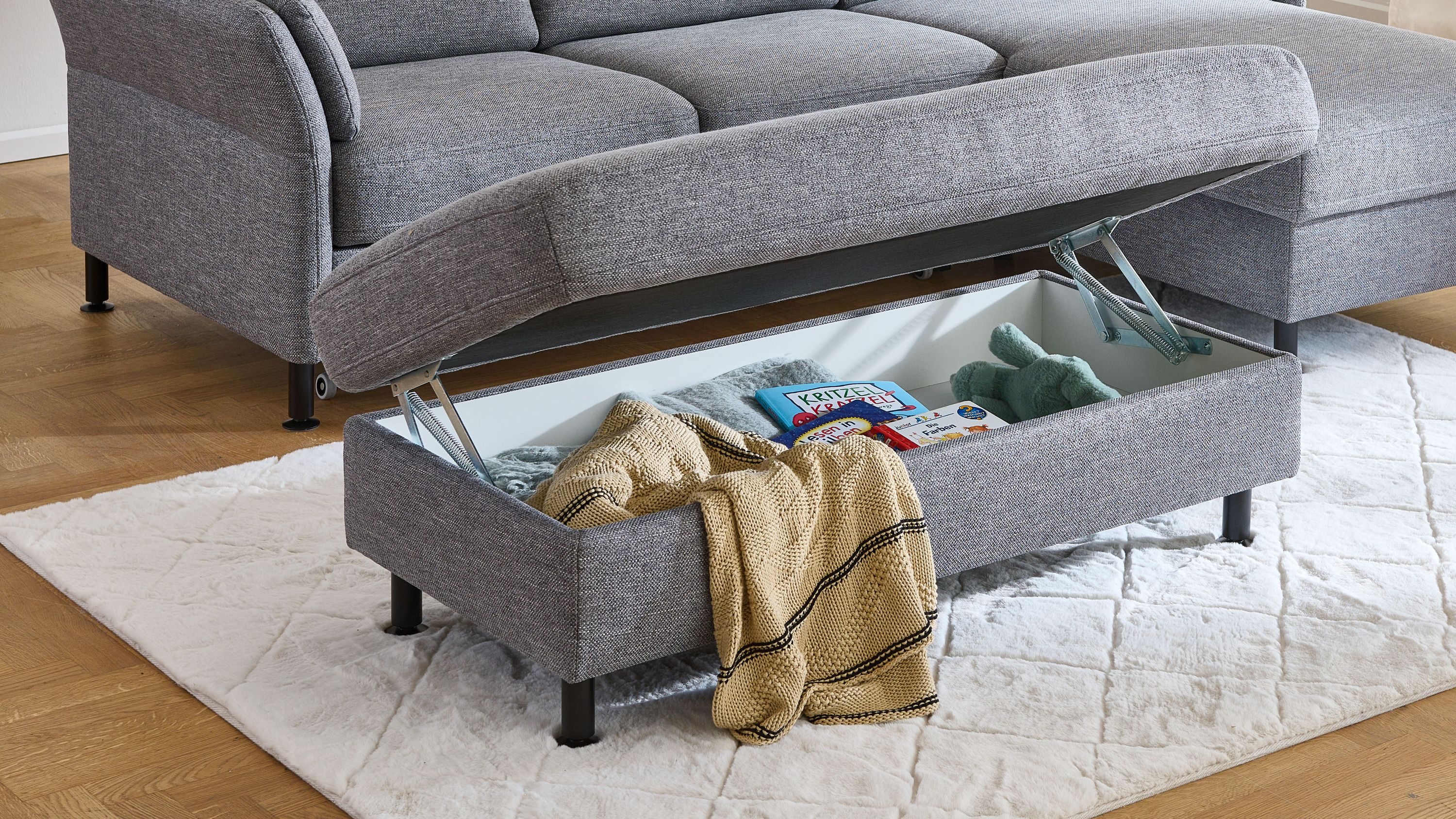 XXL-Hocker in stahlgrauem Flachgewebe mit schwarzer Metallstruktur und aufklappbarem Stauraum