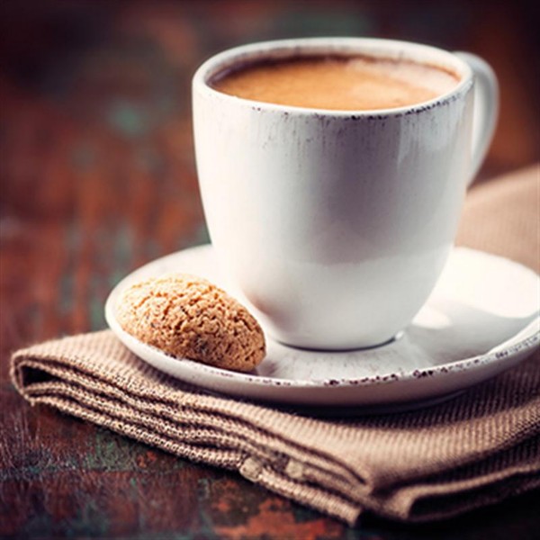 Von schräg oben: Weiße Tasse mit Kaffee auf Untertasse, daneben ein runder Keks auf brauner, gefalteter Serviette