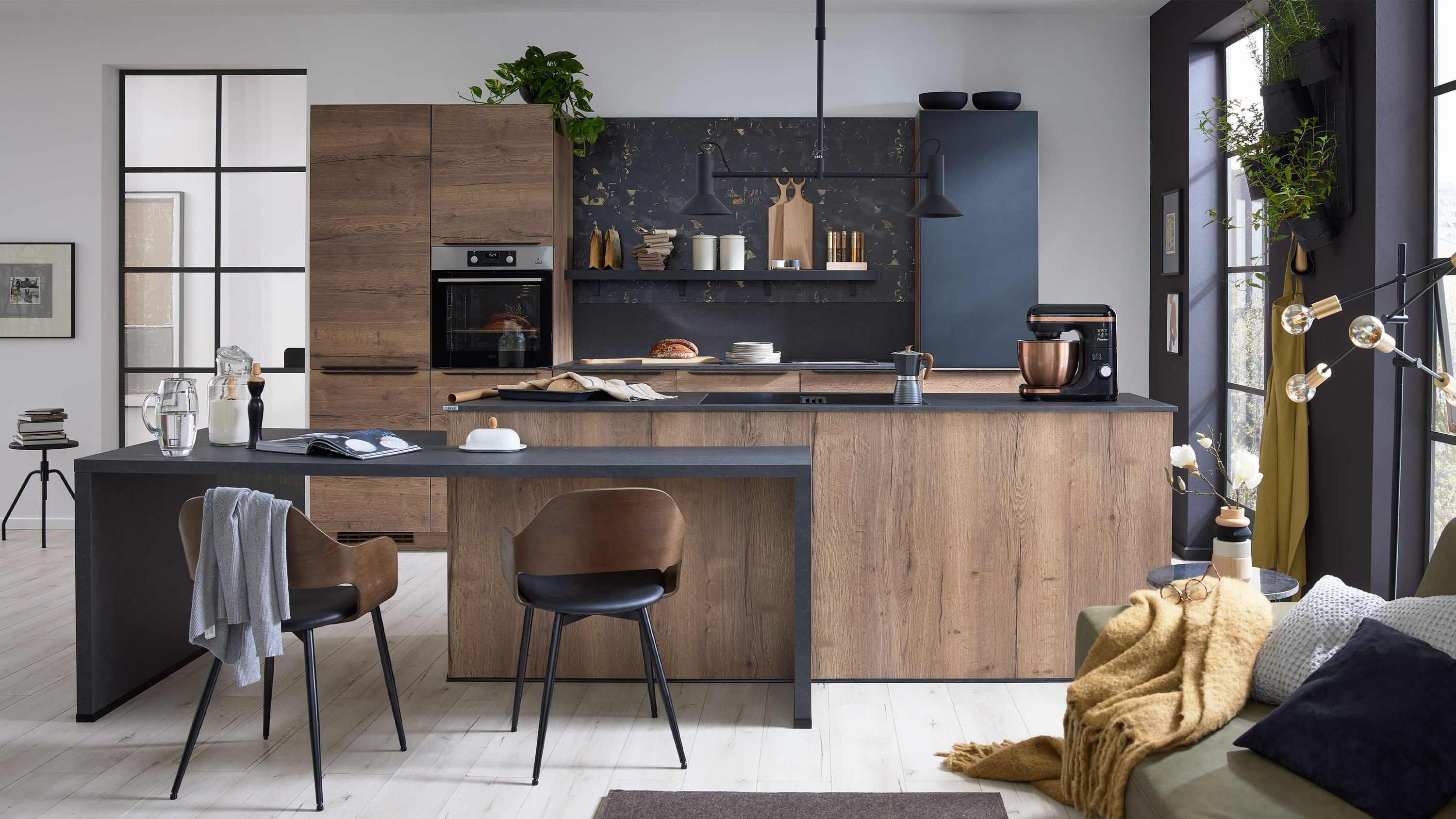 Holzfronten schwarze Arbeitsplatte Barhocker; Sofa mit Kissen Deko helle Atmosphäre durch große Fenster
