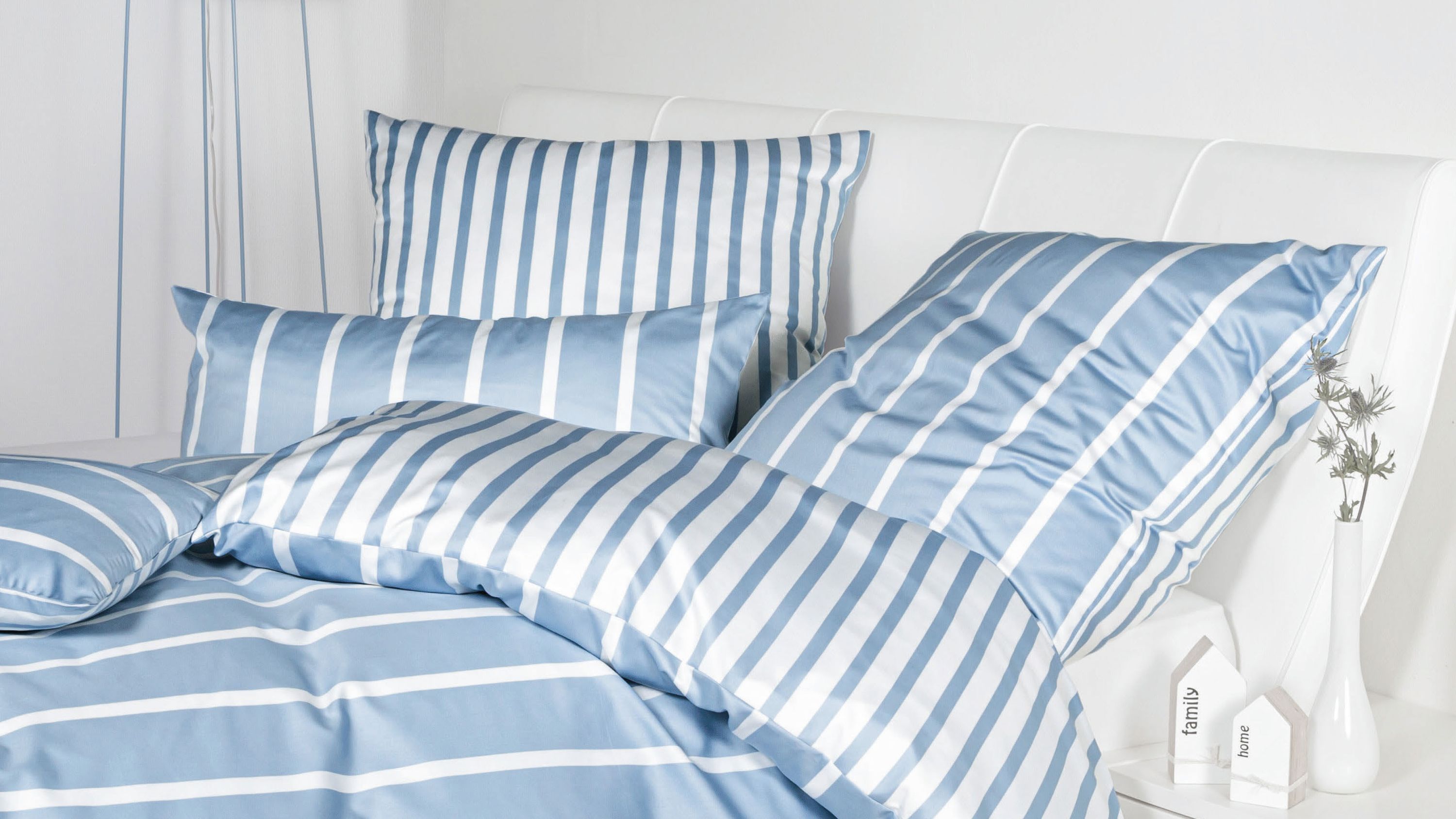 Bettwäsche-Set mit blauen und weißen Streifen auf Bett mit weißem Kopfteil