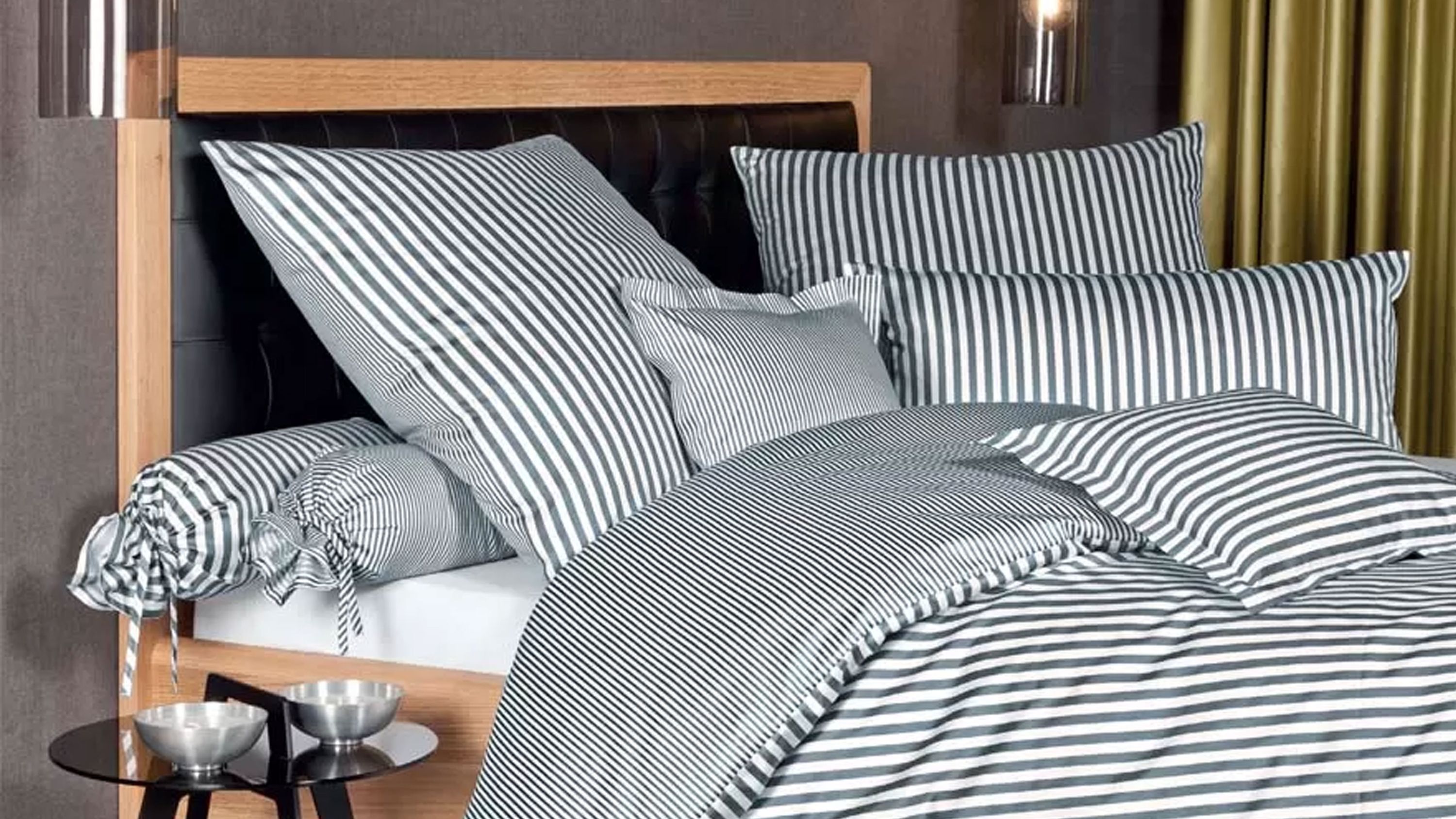 Bett mit gestreifter Bettwäsche in weiß und anthrazit mit mehreren Kissen und Zierrollen