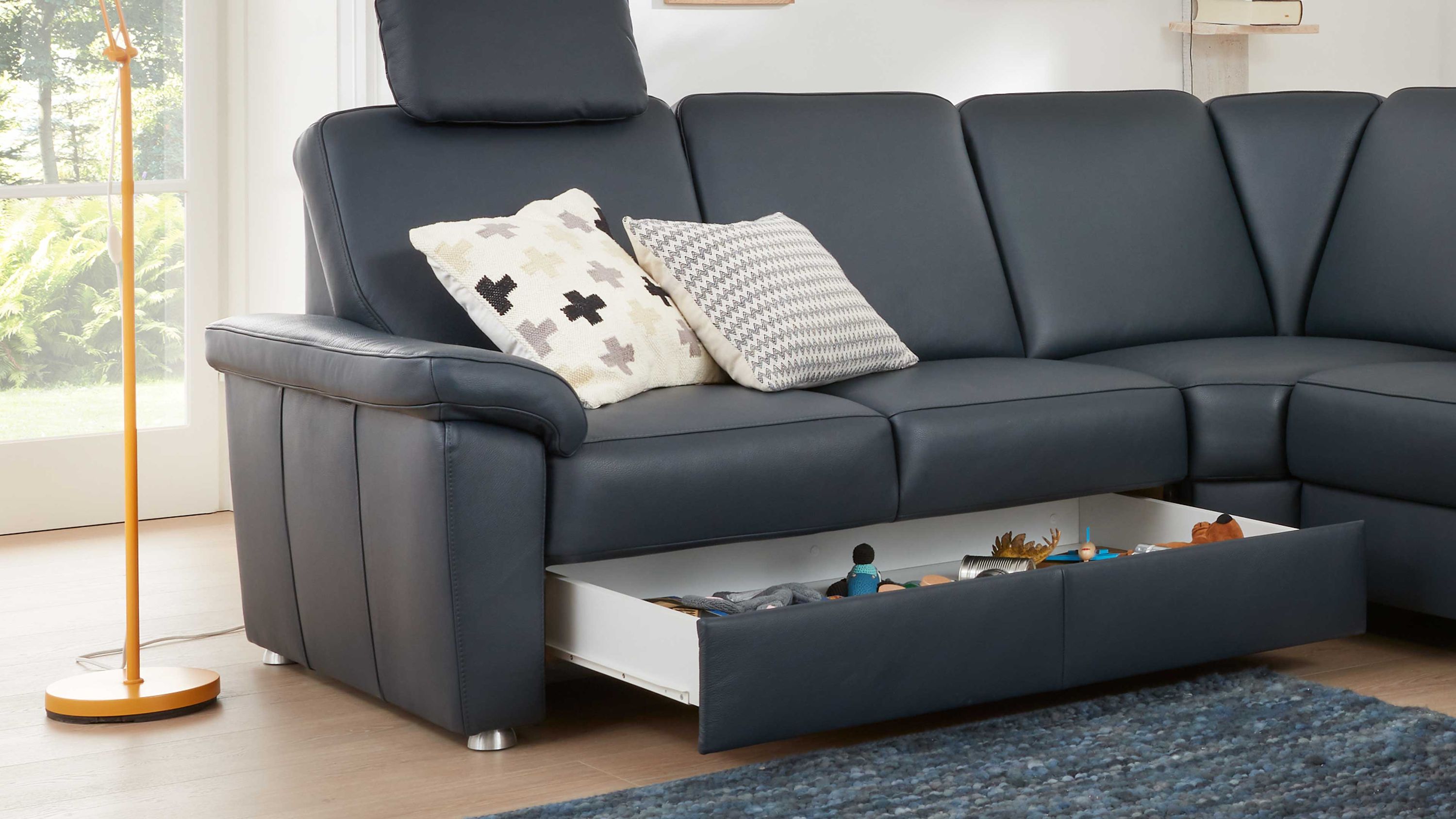 Schwarzes Ecksofa mit zwei gemusterten Kissen und geöffneter Schublade unter der Sitzfläche