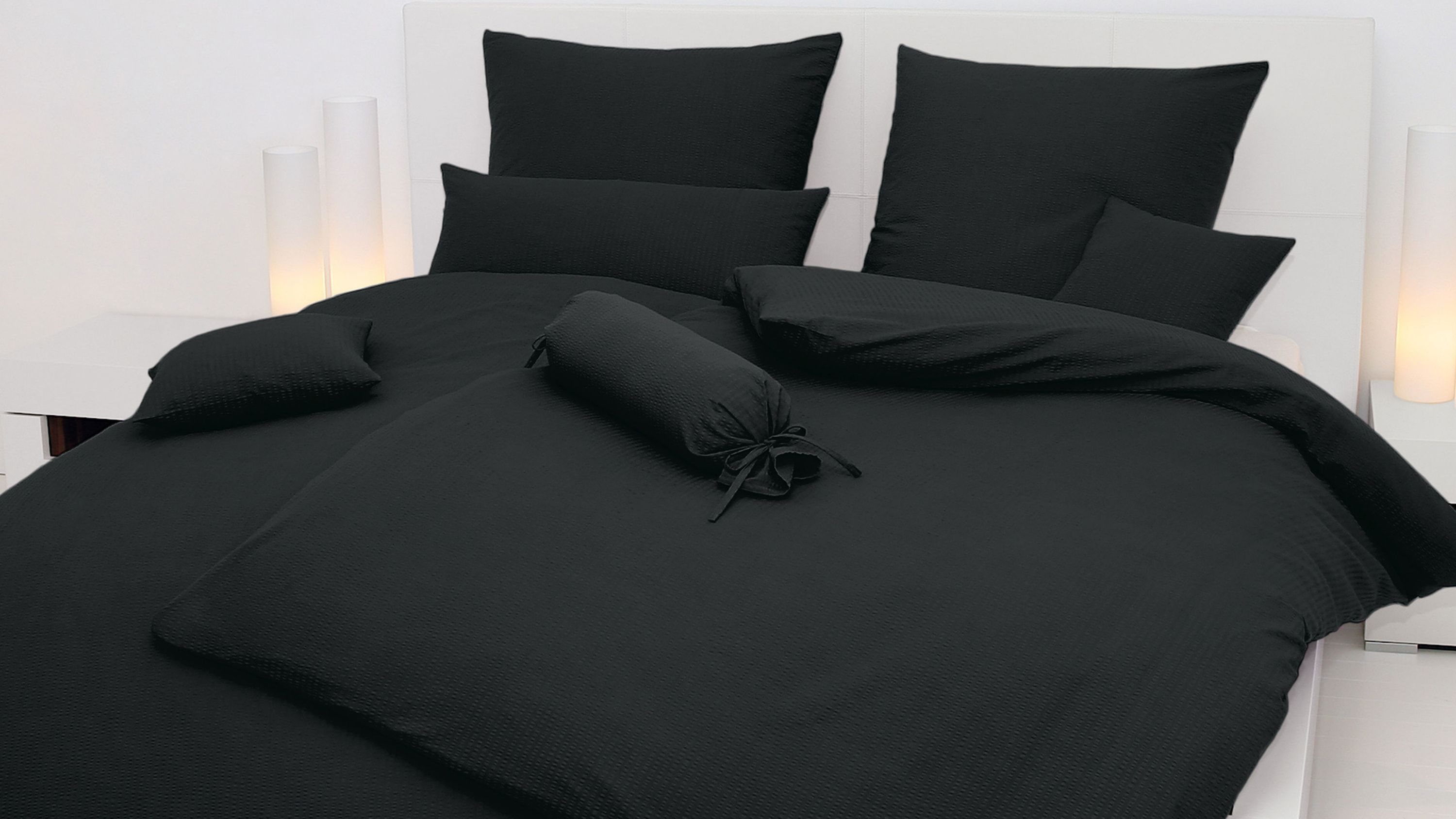 Schwarzes Bettwäsche-Set mit Kissen und Bettbezug auf weißem Bett in modernem Schlafzimmer
