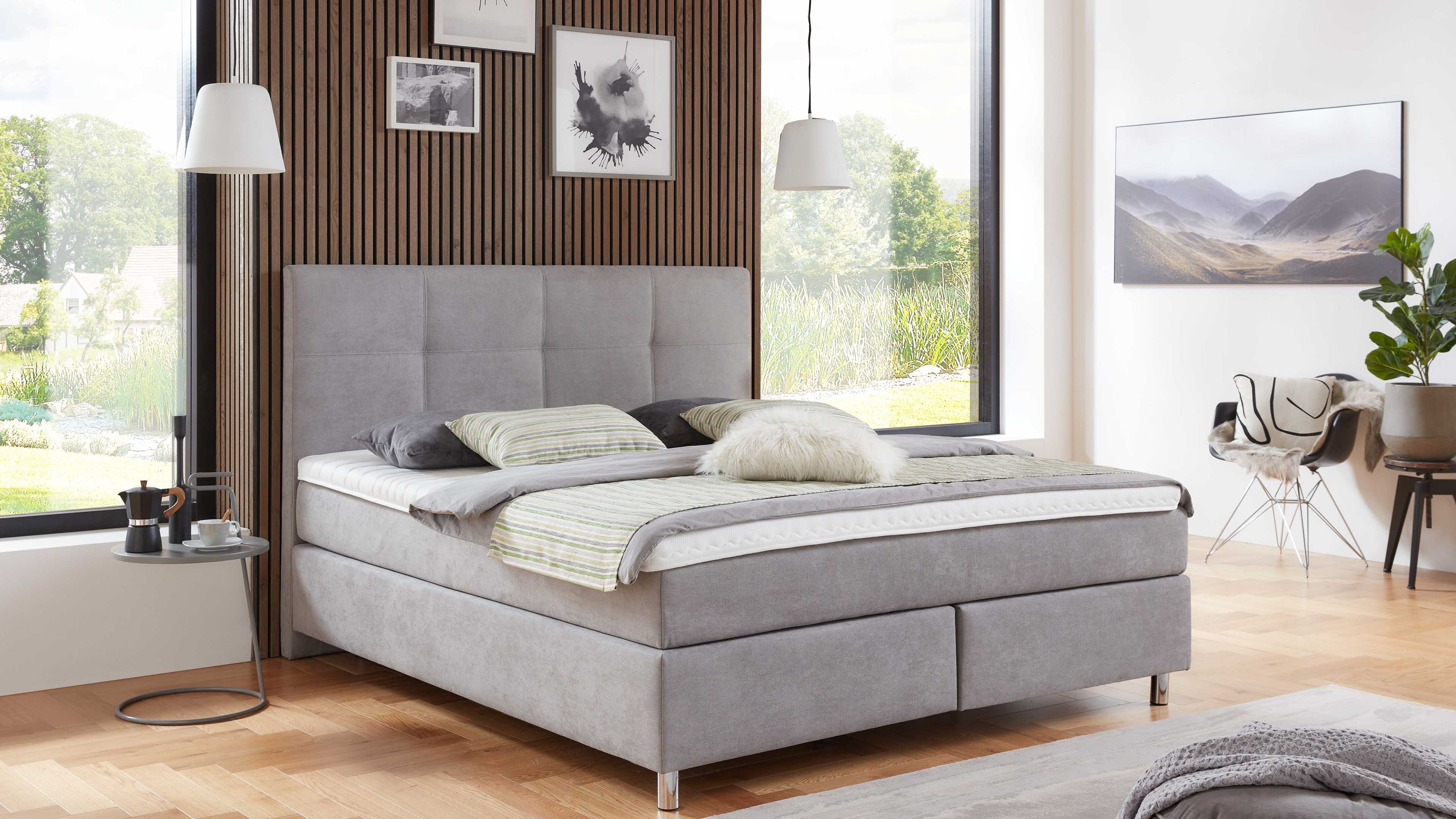 Hellgraues Boxspringbett mit gepolstertem Kopfteil und silbernen Beinen in modernem Schlafzimmer