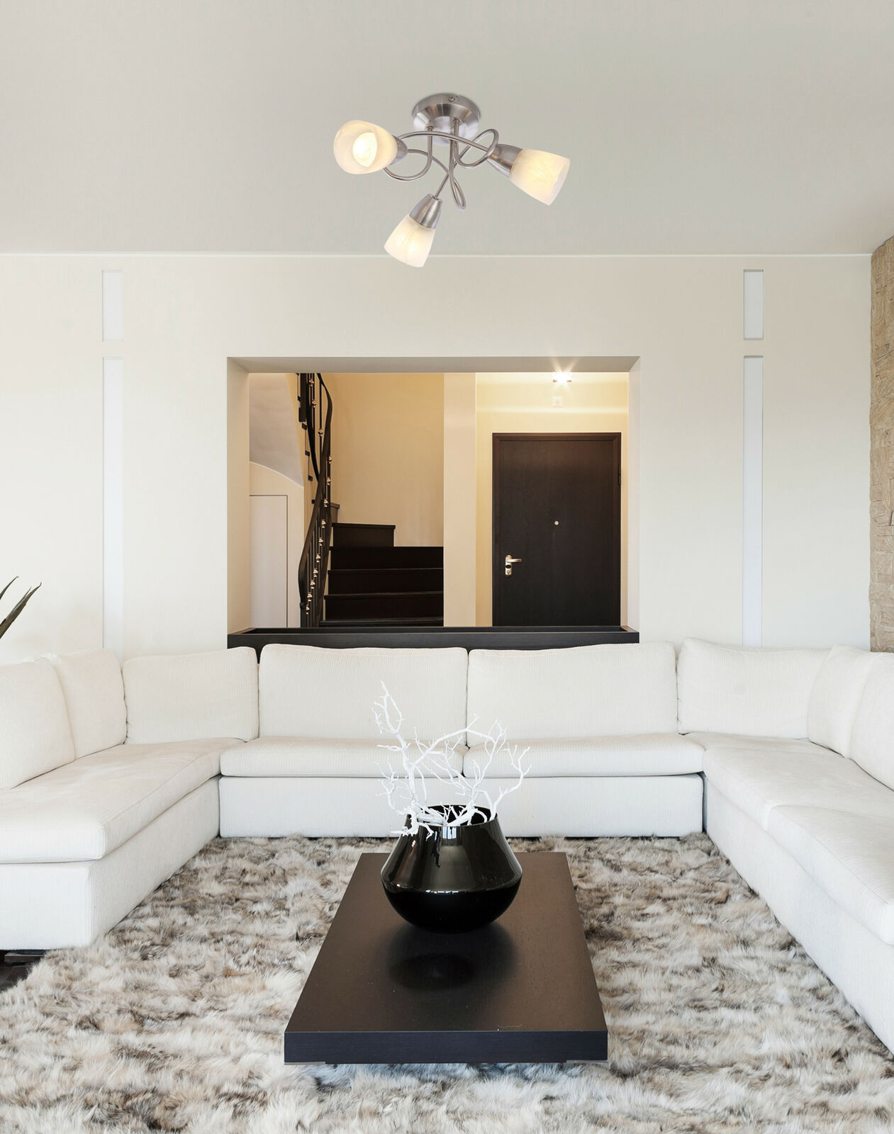 Wohnzimmer mit weißem Ecksofa, schwarzem Couchtisch, hellem Teppich und Deckenleuchte mit drei Strahlern