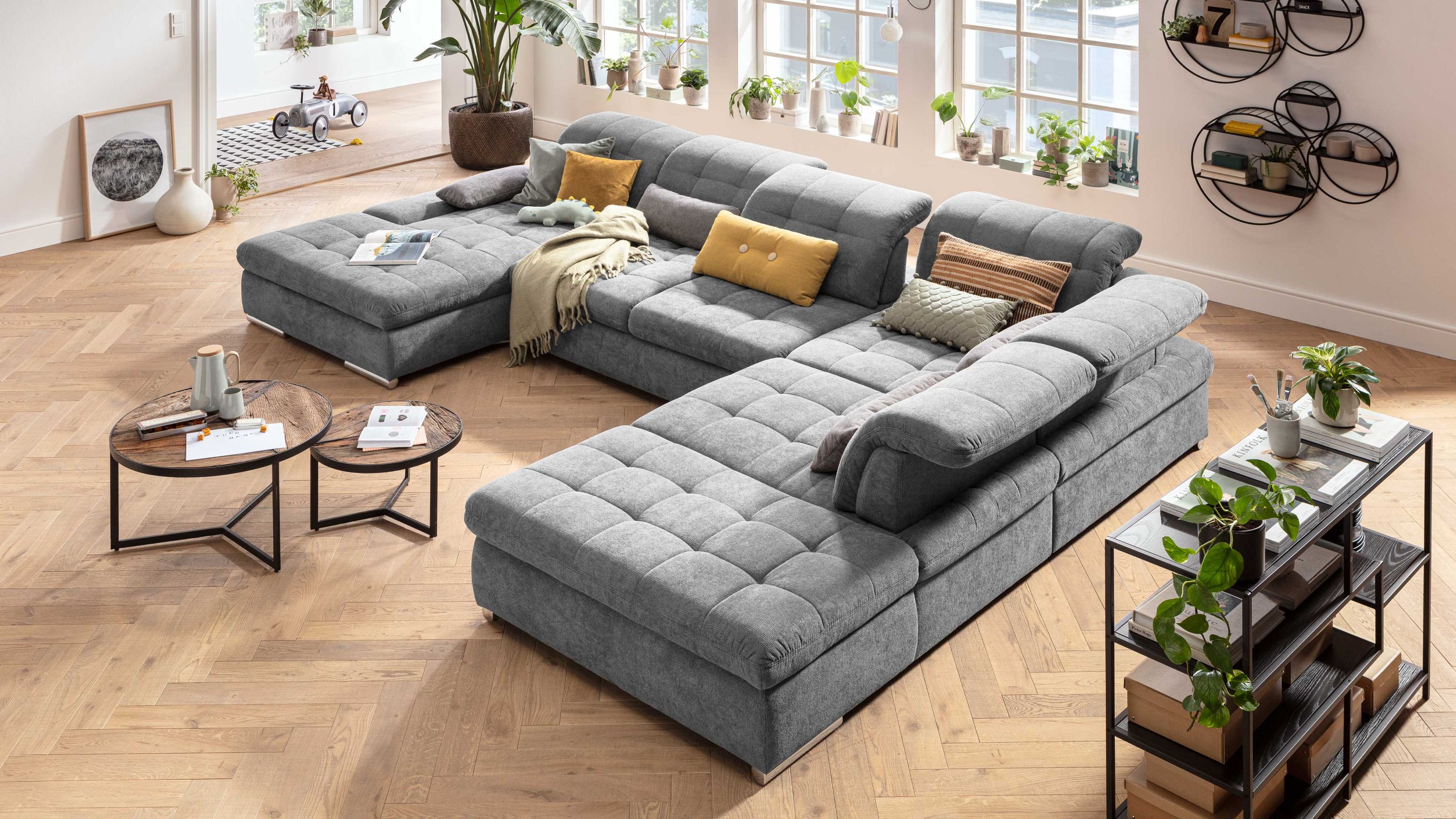 Großes graues Ecksofa mit verstellbaren Rückenlehnen und Chromfüßen in hellem Raum mit Holzboden