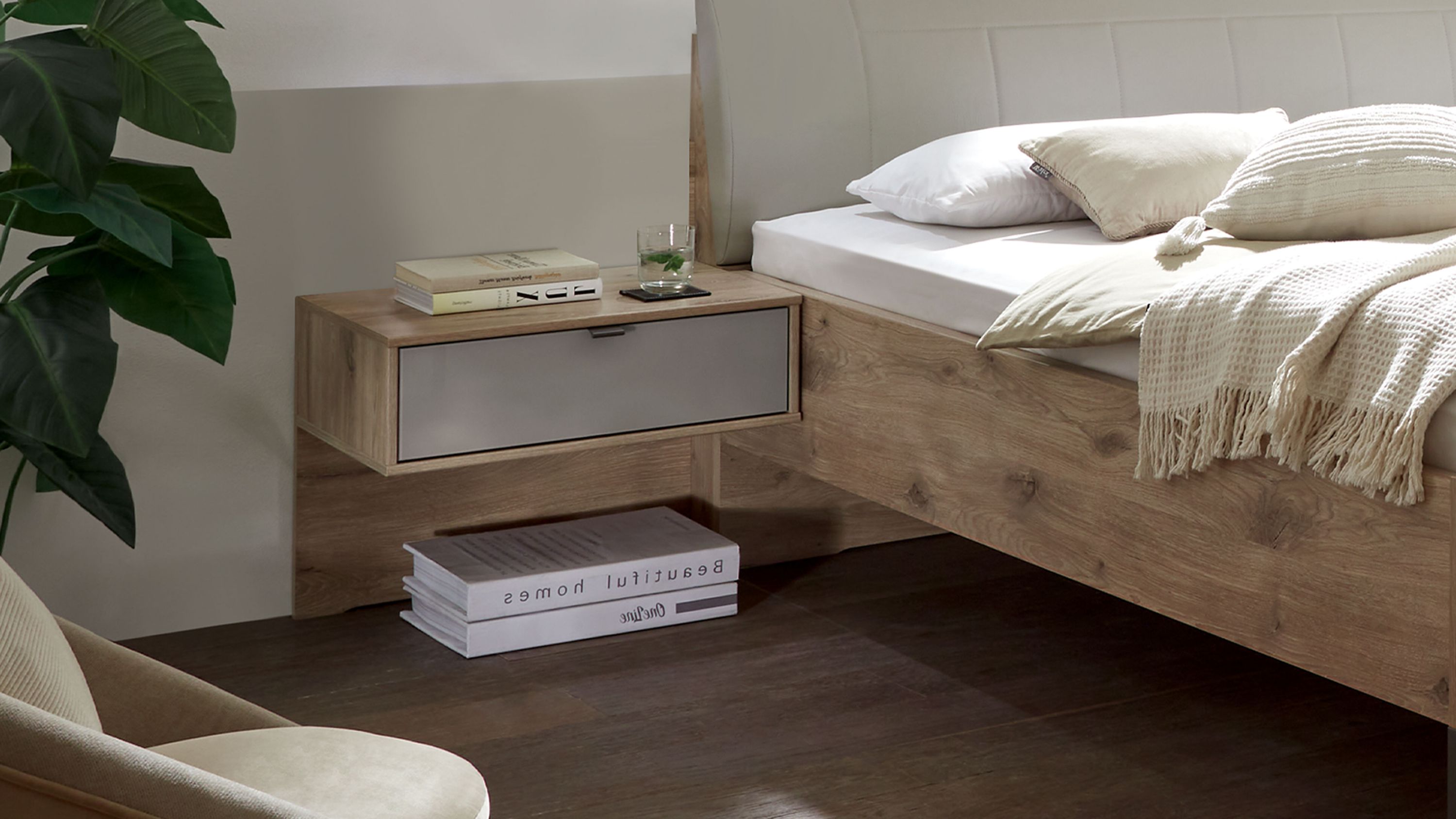 Zweiteilige Hängekonsole mit Schublade in grauer Front und Holzoptik an Wand neben Bett mit Holzkorpus