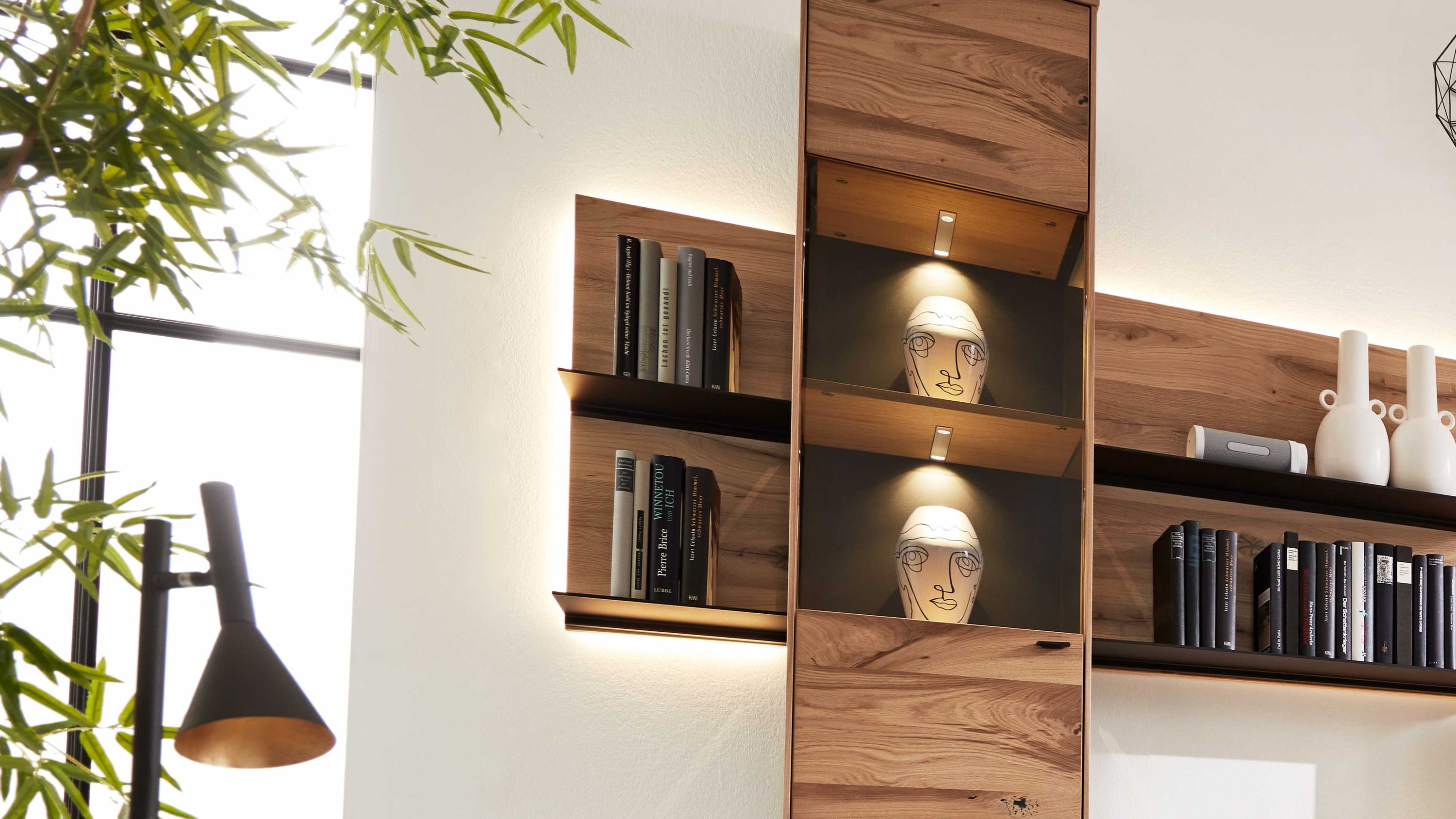 Wandpaneel mit Regalen aus Holz in brauner Farbe und schwarzen Rückwänden beleuchtet mit Büchern und Dekoration
