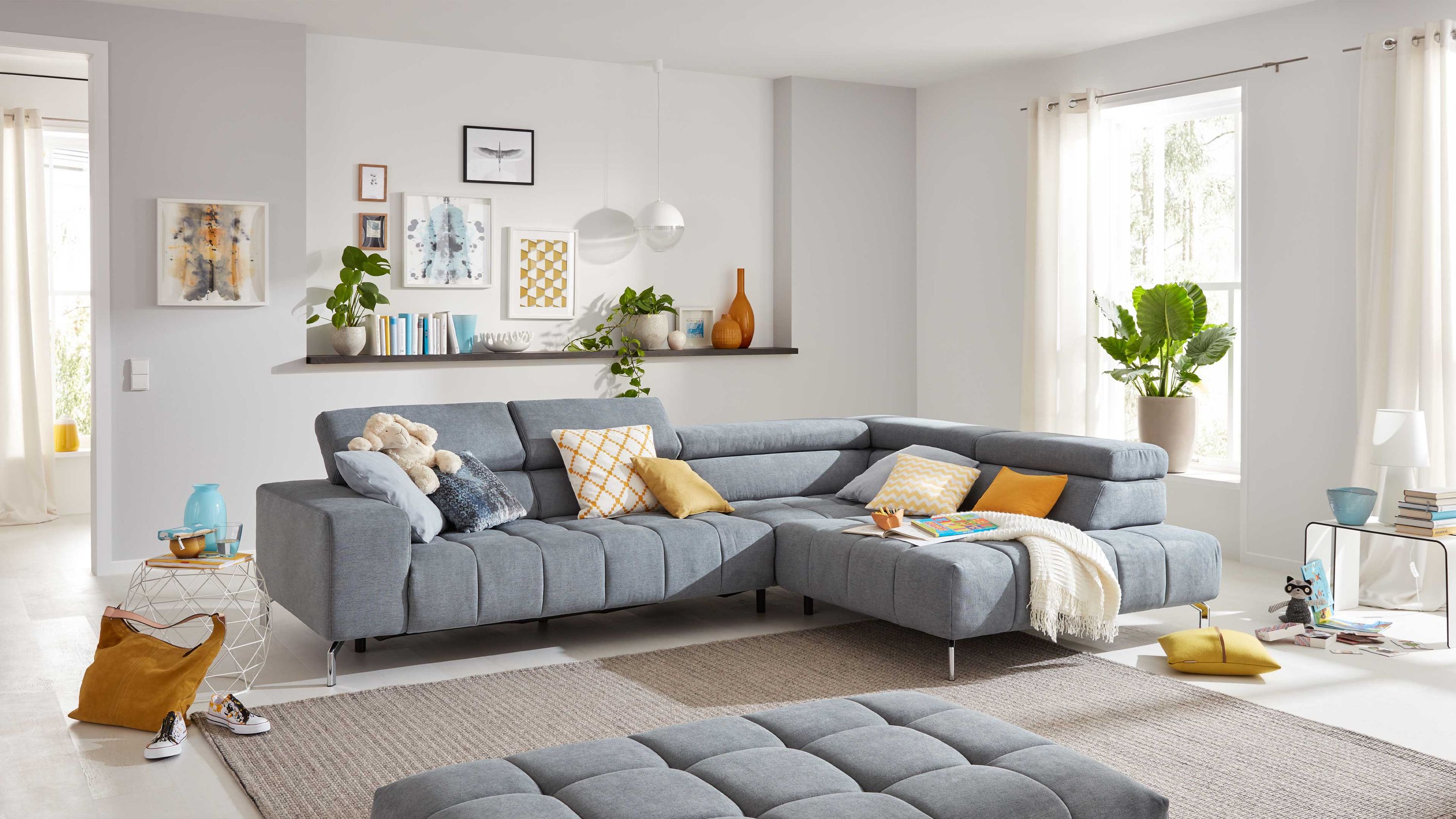 Ecksofa mit chromfarbenen Füßen und grauem Stoffbezug in modernem Wohnzimmer mit Kissen und Decke