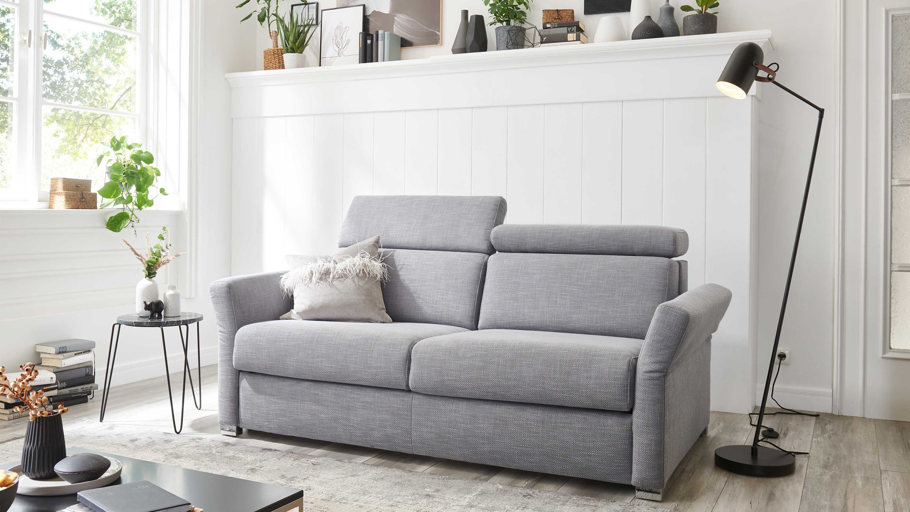 Graues Schlafsofa mit verstellbaren Kopfstützen und Chromfüßen in hellem Wohnzimmer