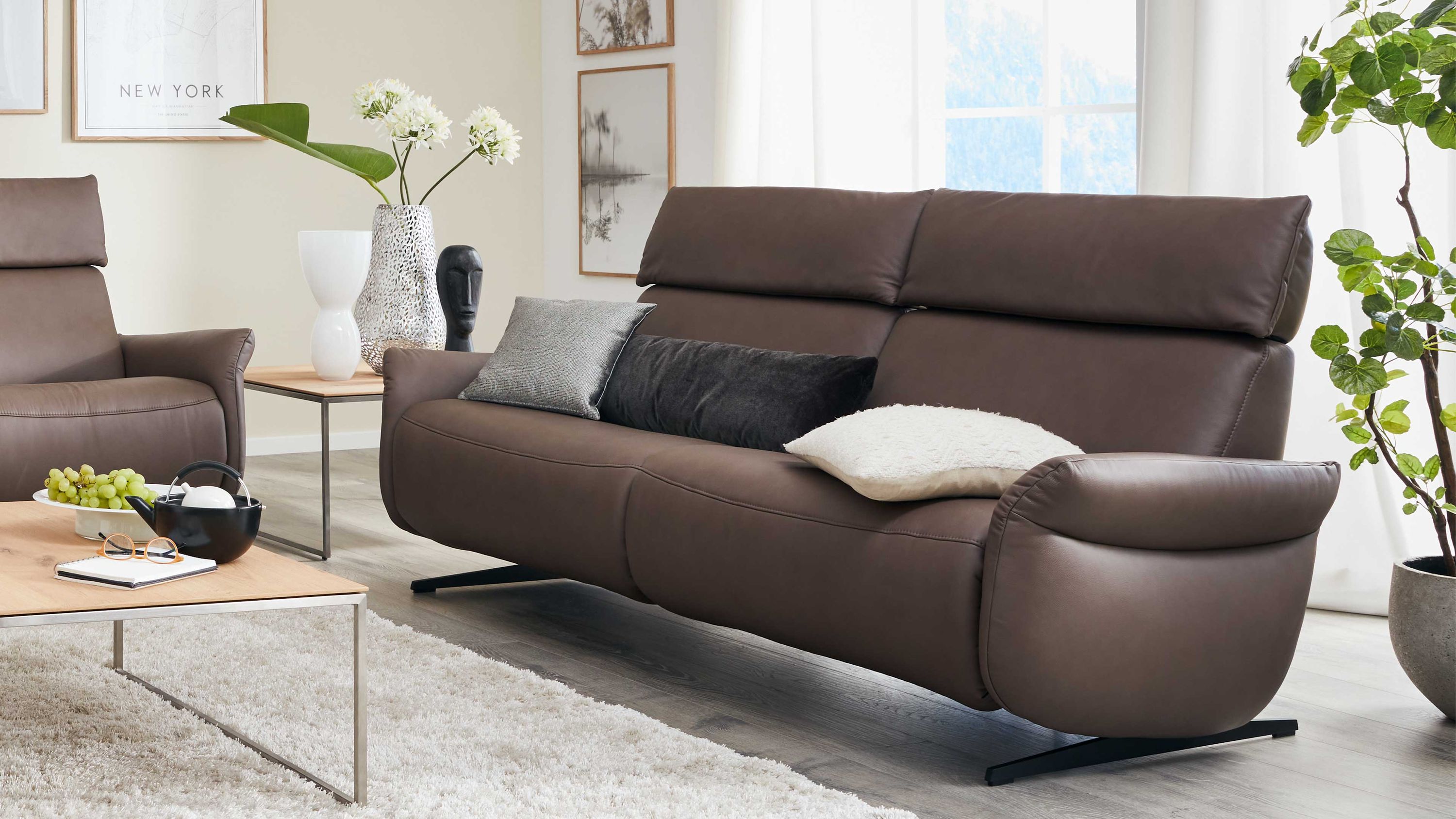 Dreisitziges Sofa in braun mit hohen Rückenlehnen und drei Kissen in einem hellen Wohnzimmer