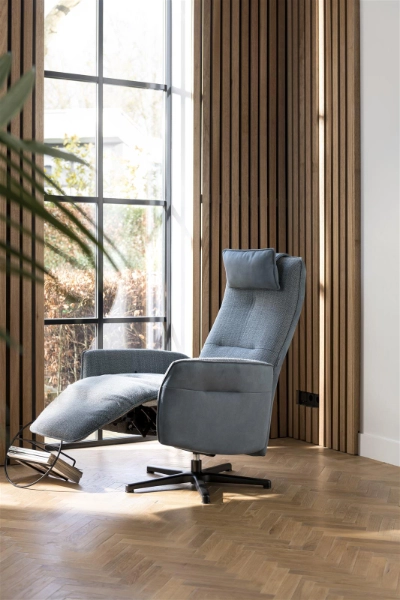 Relaxsessel mit Ausblick im stilvollen Wohnzimmer. Moderner Relaxsessel in Grau mit verstellbarer Fußstütze steht vor bodentiefem Fenster und Holzlamellenwand.