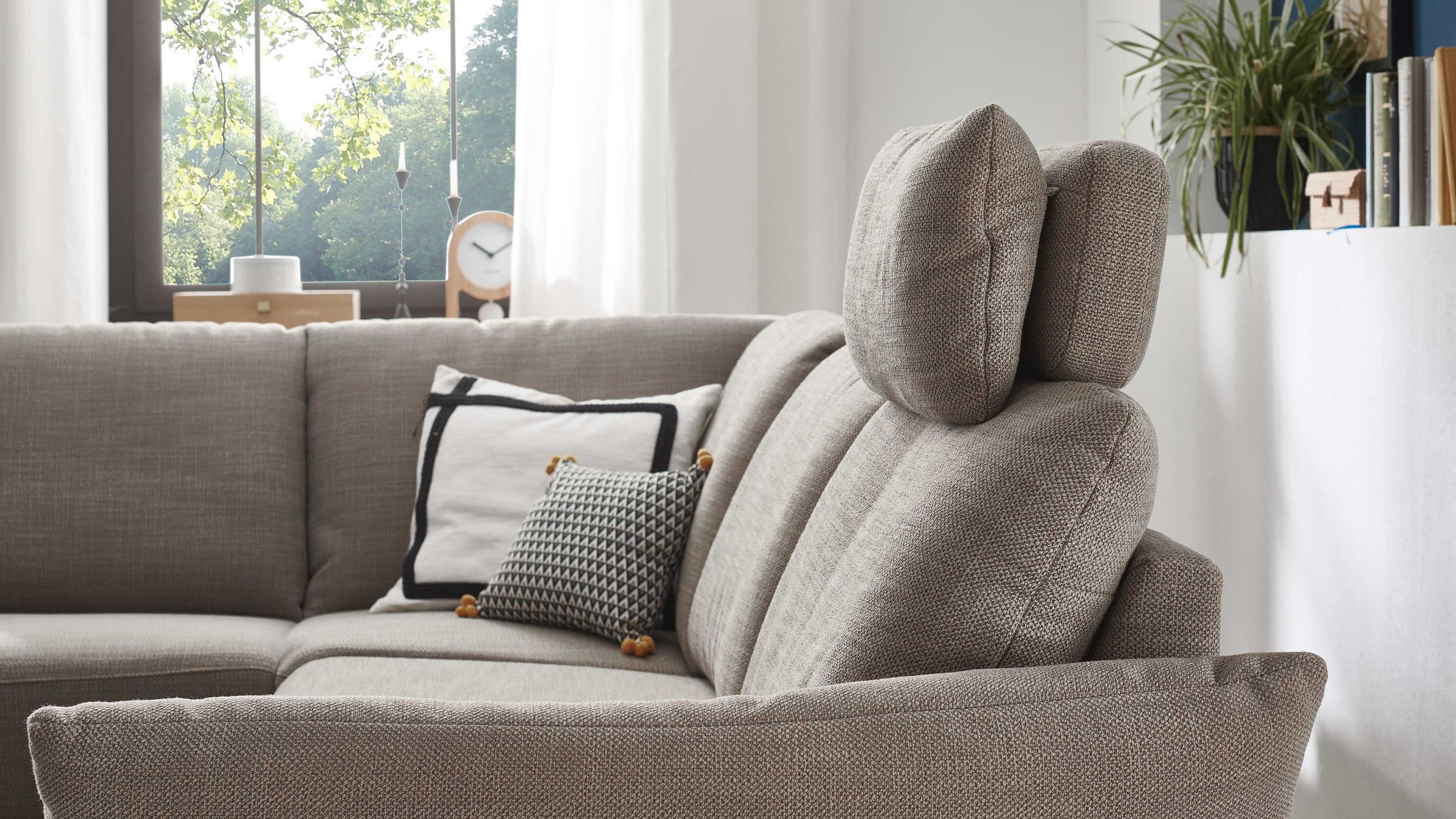 Ecksofa mit taupefarbenem Flachgewebe und verstellbarer Kopfstütze in einem hellen Wohnraum