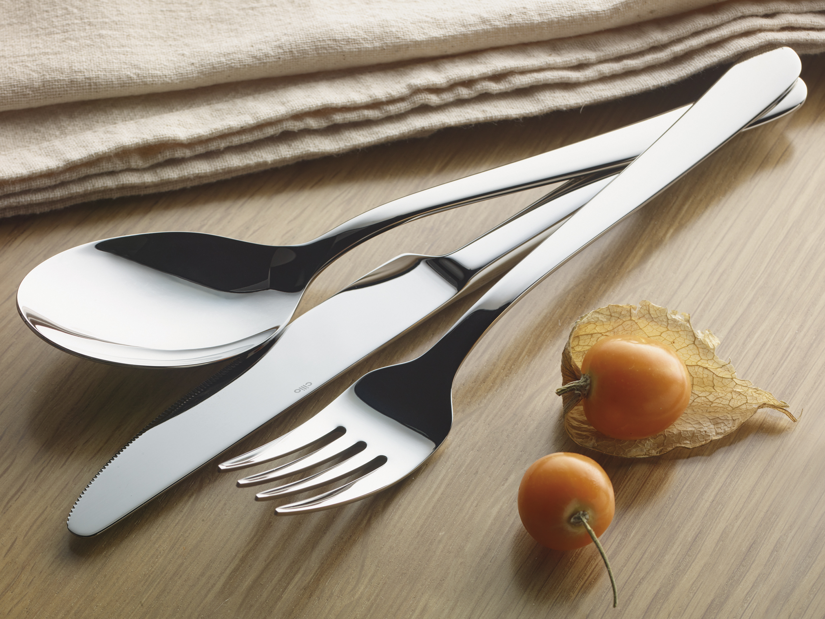 Set aus Löffel Messer und Gabel aus glänzendem Edelstahl auf Holzoberfläche mit zwei orangefarbenen Früchten