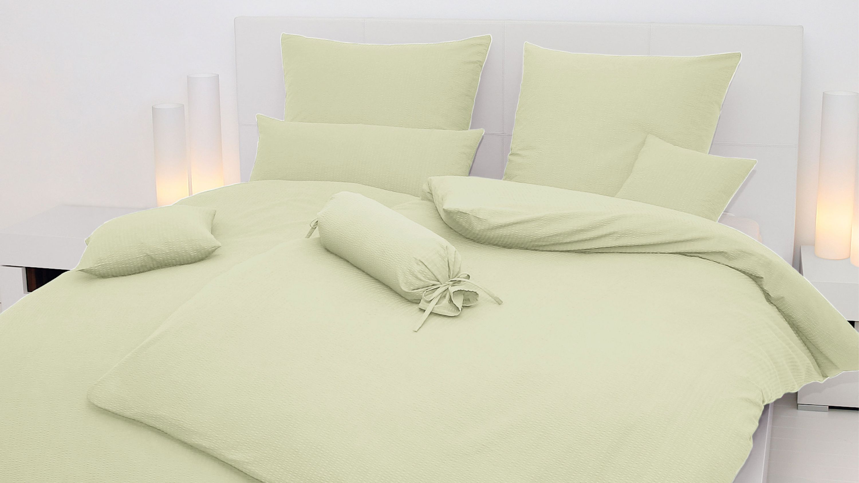 Hellgrüne Bettwäsche mit Kissen und Nackenrolle auf weißem Bett mit Kopfteil