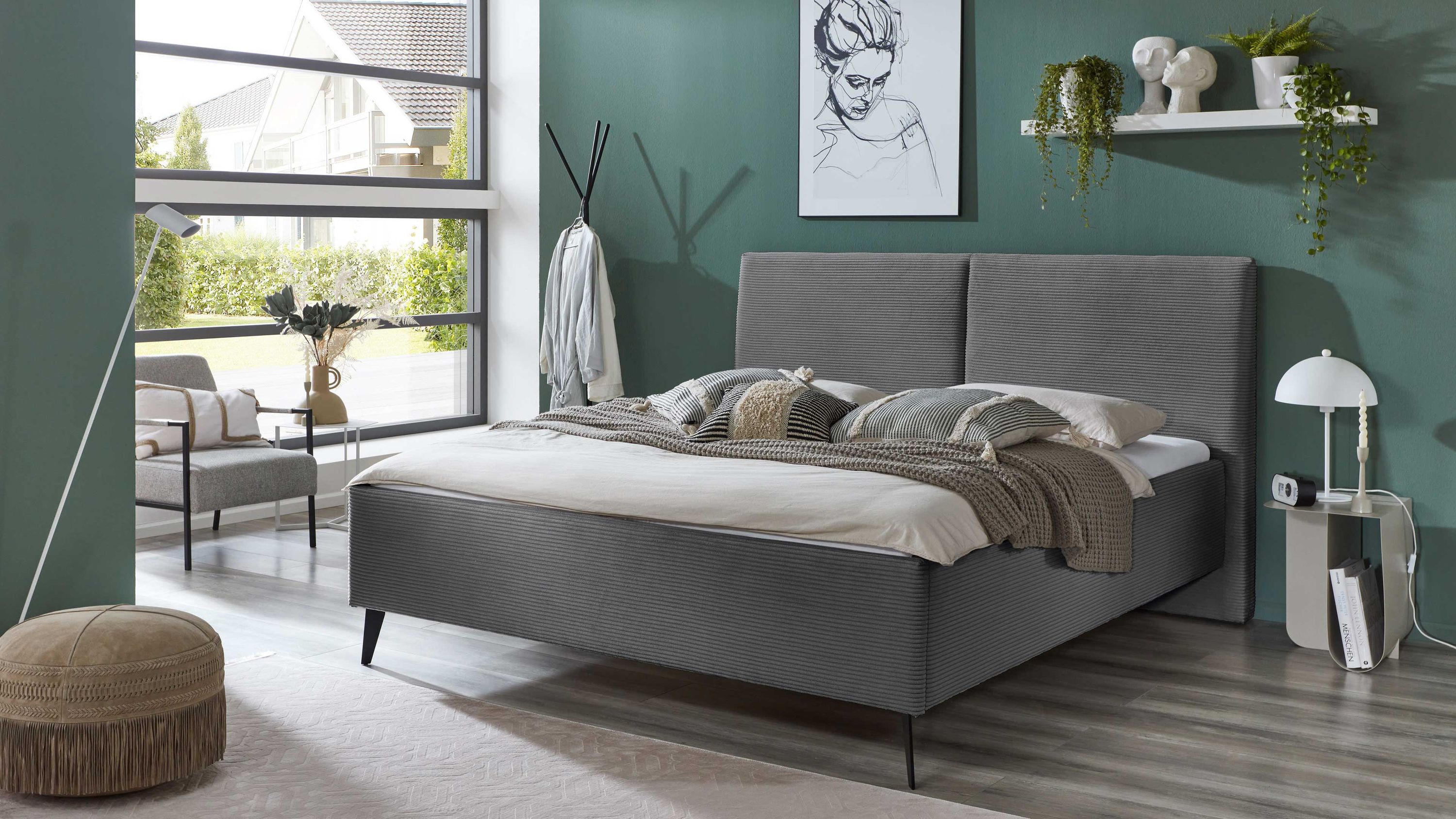 Graues Polsterbett mit breitem Kopfteil und schwarzen Metallfüßen in modernem Schlafzimmer