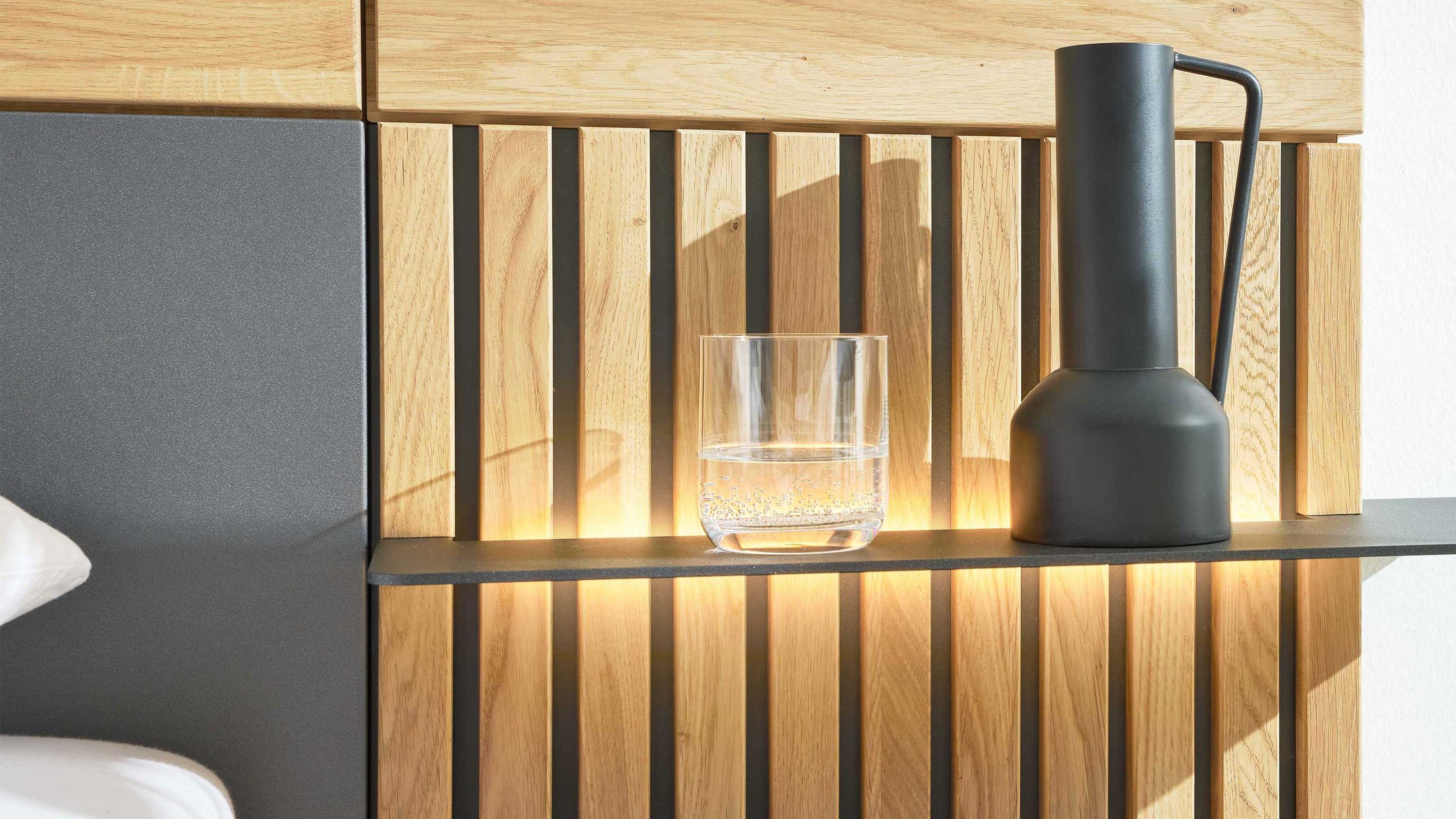 Holzpaneel mit vertikalen Lamellen und integrierter Beleuchtung schwarzes Regalbrett mit Glas und Karaffe