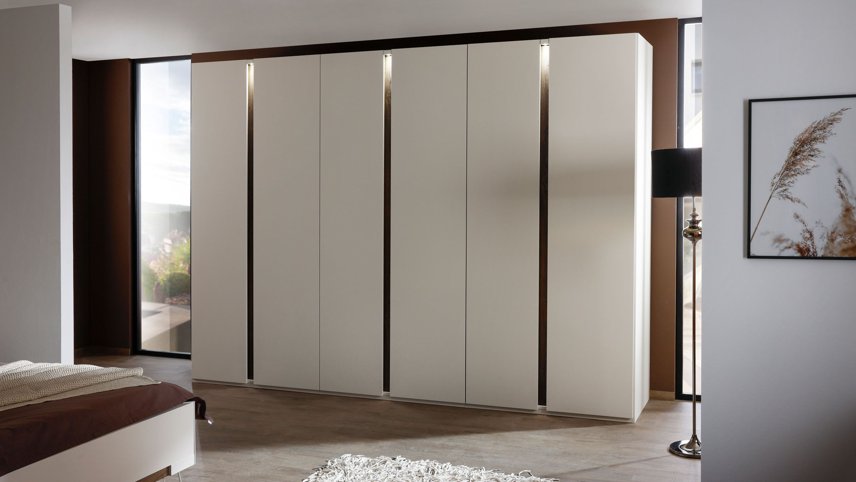 Kleiderschrank mit sechs Türen und Beleuchtung in champagnerfarben Sechstüriger Kleiderschrank in champagnerfarben mit vertikalen Beleuchtungsstreifen in einem Schlafzimmer