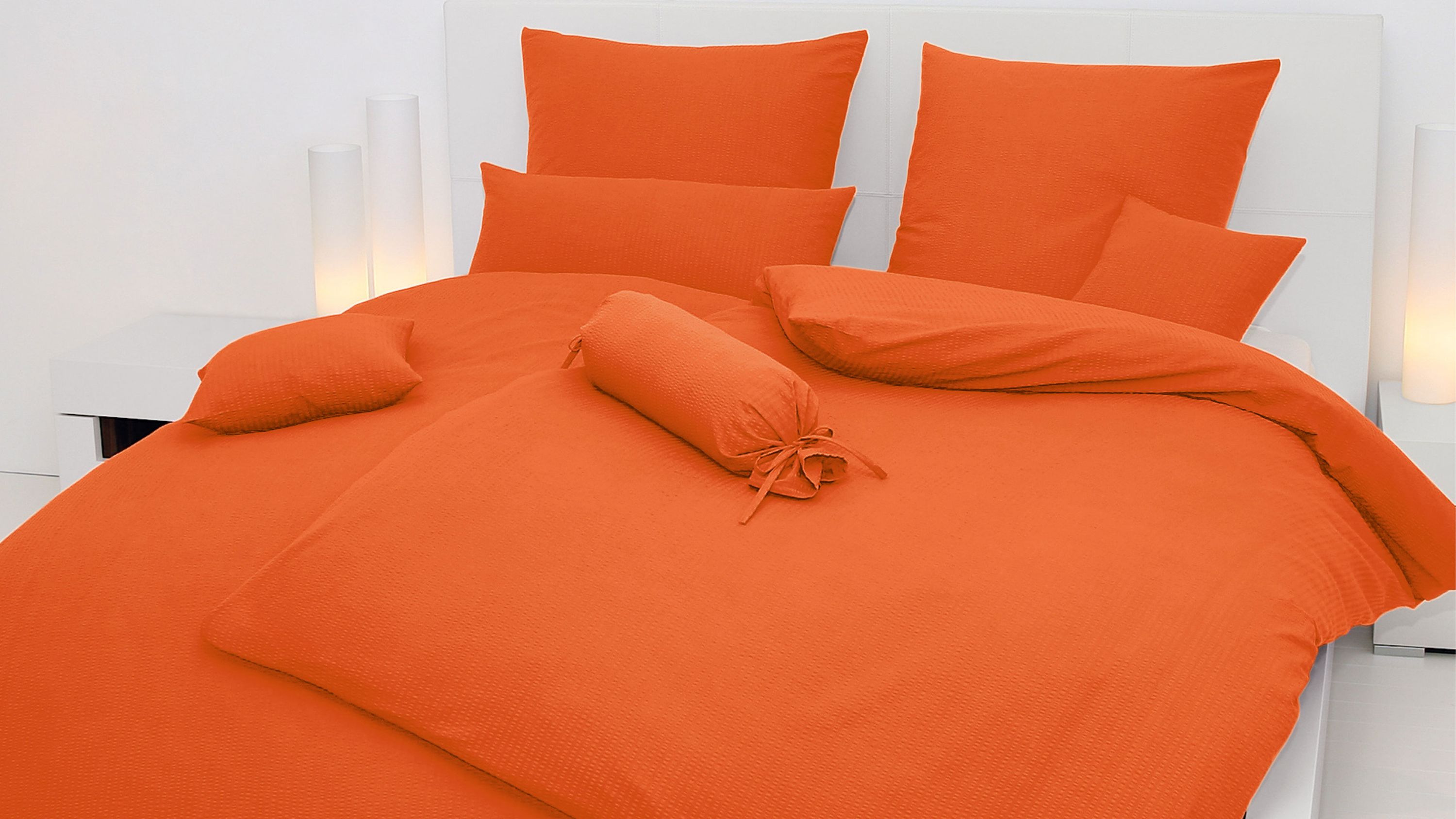 Oranges Bettwäsche-Set mit Kissen und Zierkissen auf weißem Bett in modernem Schlafzimmer
