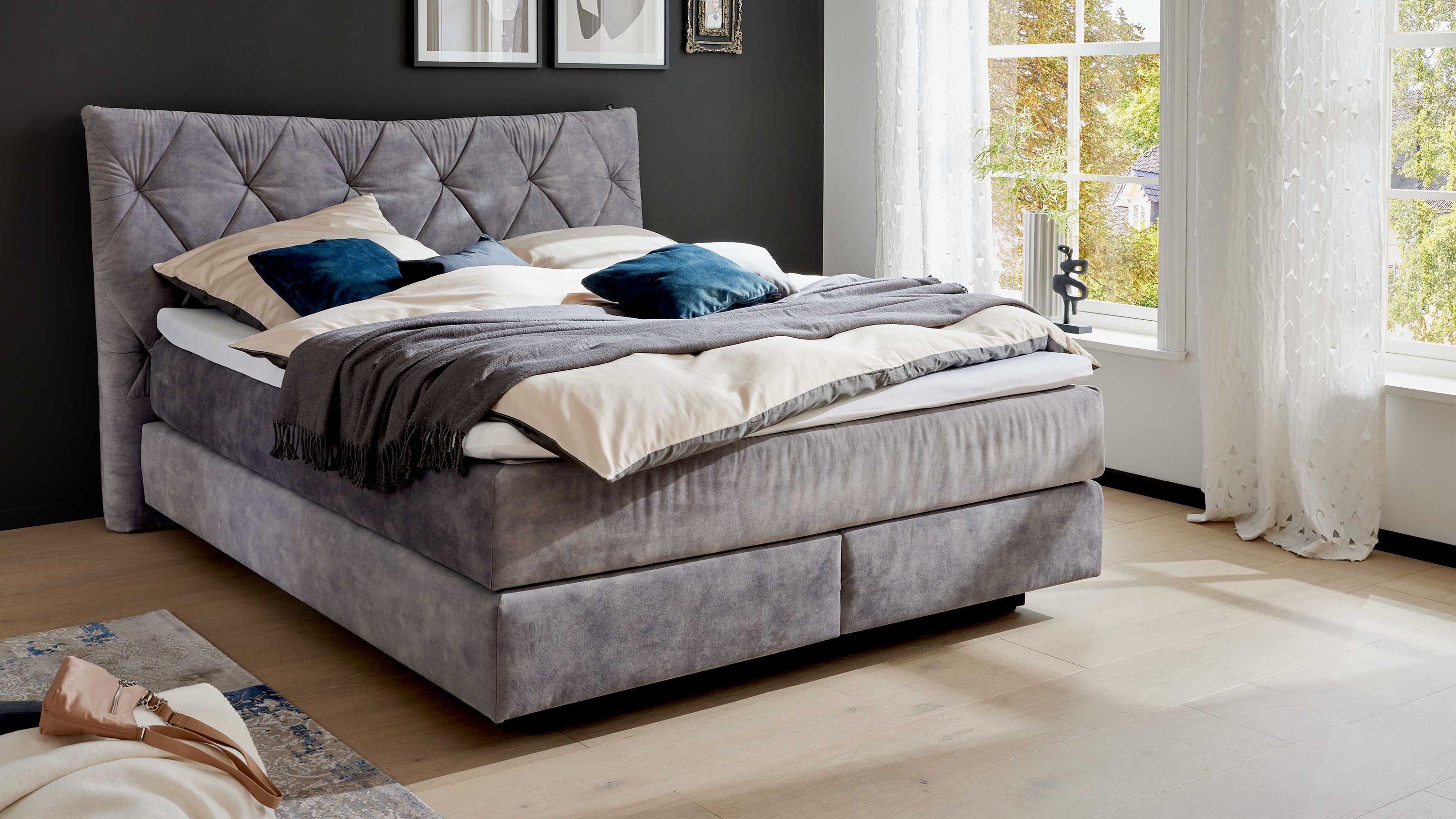 Boxspringbett mit hohem Kopfteil und Bettkasten in silberfarbenem Stoff in einem hellen Schlafzimmer