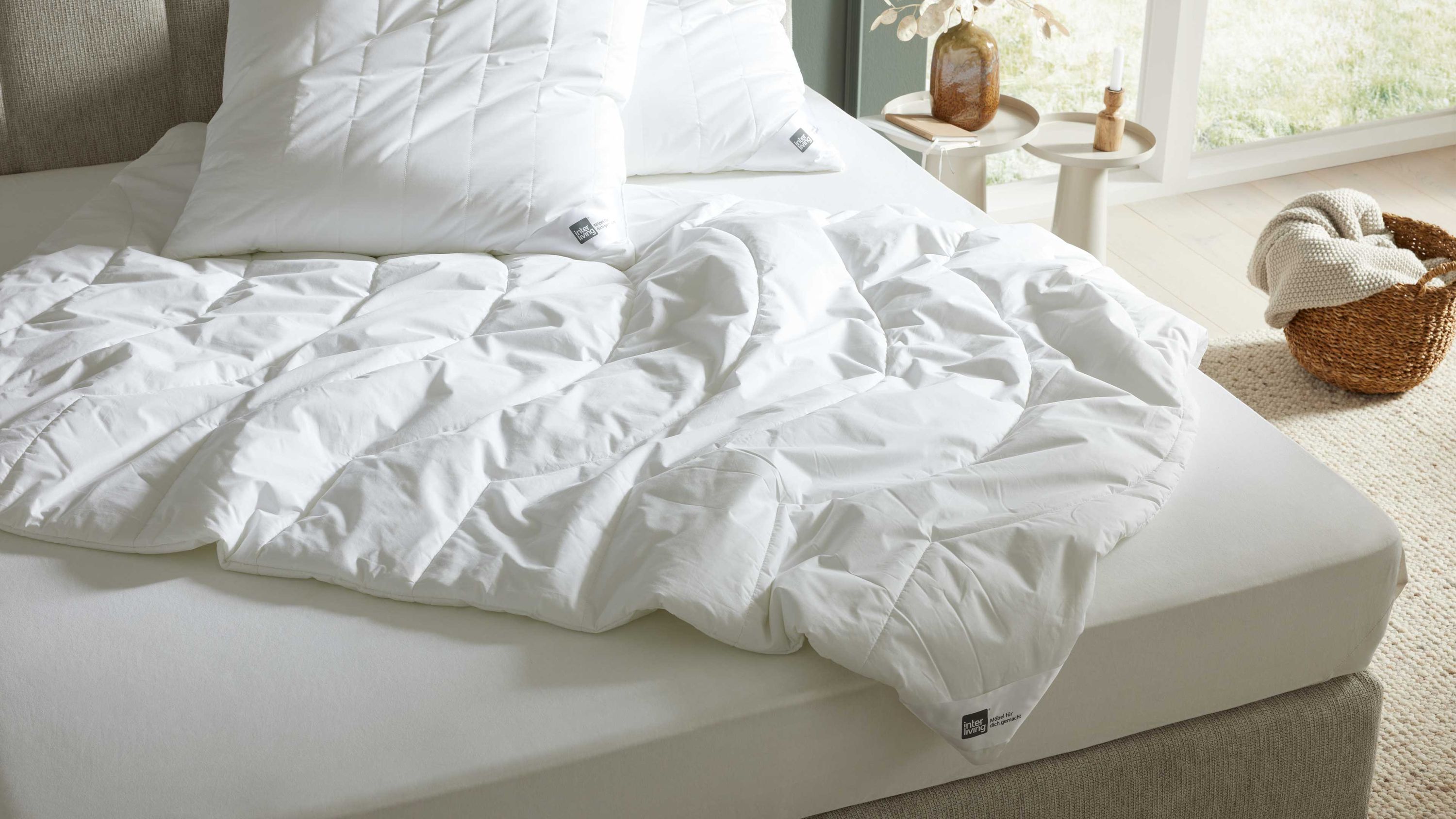 Weiße Bettdecke mit Steppmuster auf einem hellen Bett mit Kissen