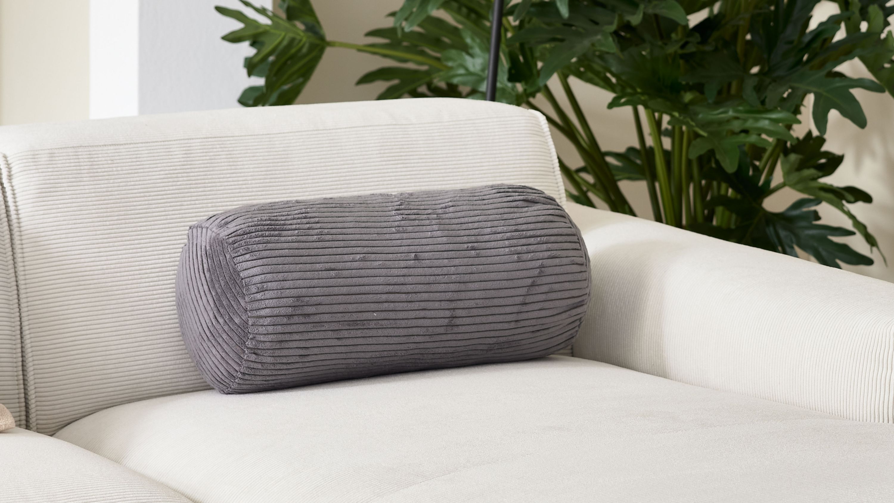 Aschegraue zylindrische Nackenrolle mit breitem Cordbezug auf weißem Sofa