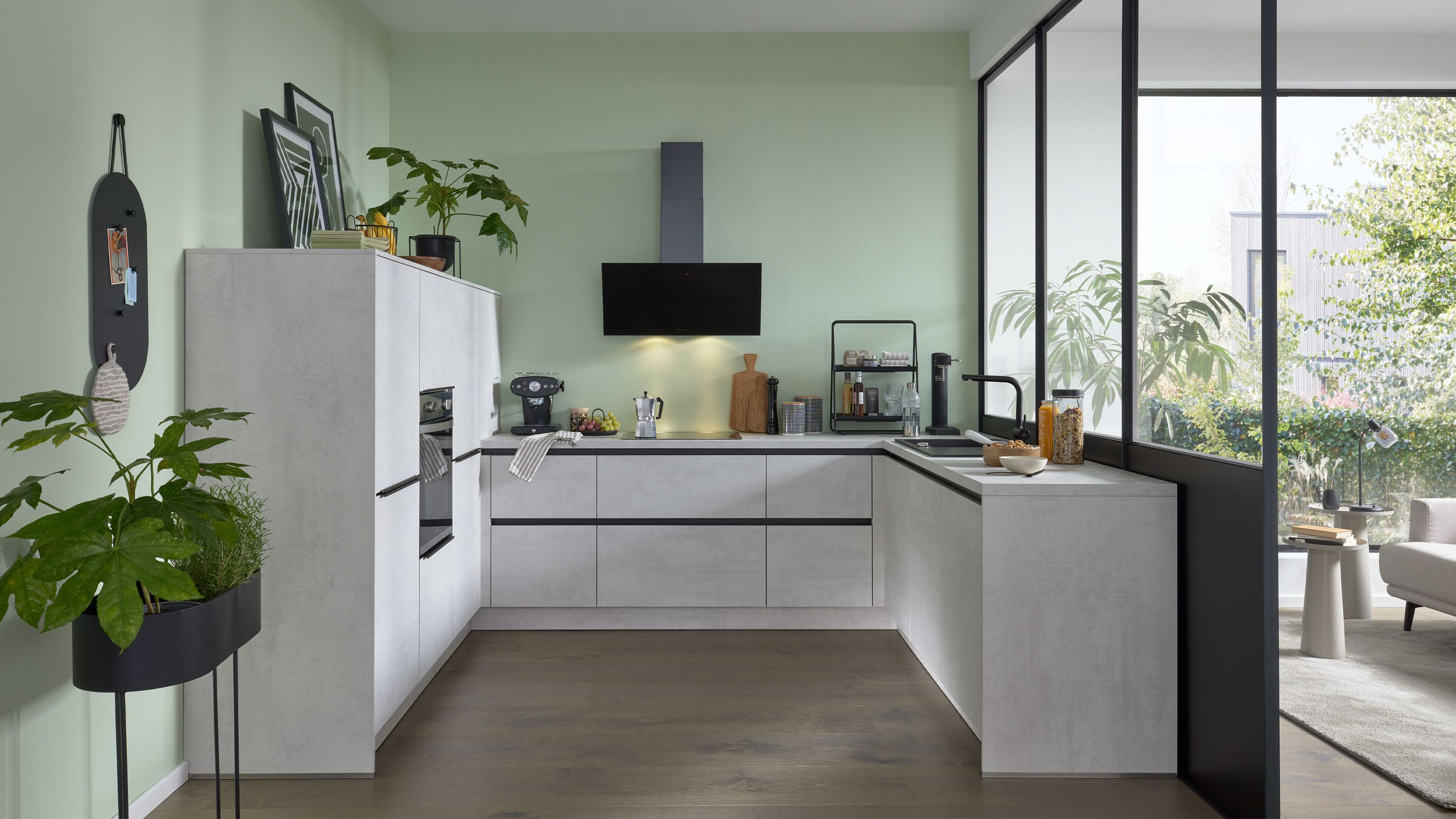 Moderne L-Küche in Betonoptik mit schwarzen Griffleisten Holzarbeitsplatte Einbauofen und Glas-Schiebetüren.