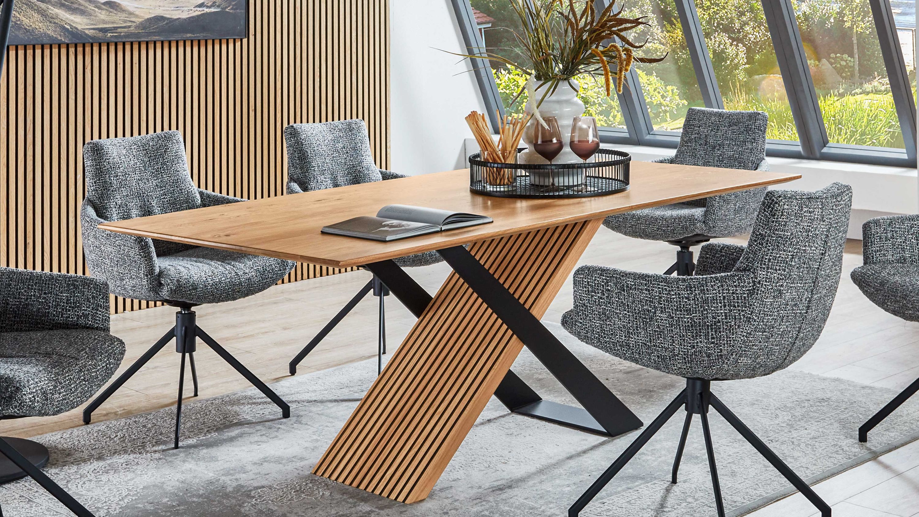 Rechteckiger Esstisch mit Holzplatte und diagonalen Holz- und Metallbeinen umgeben von grauen gepolsterten Stühlen