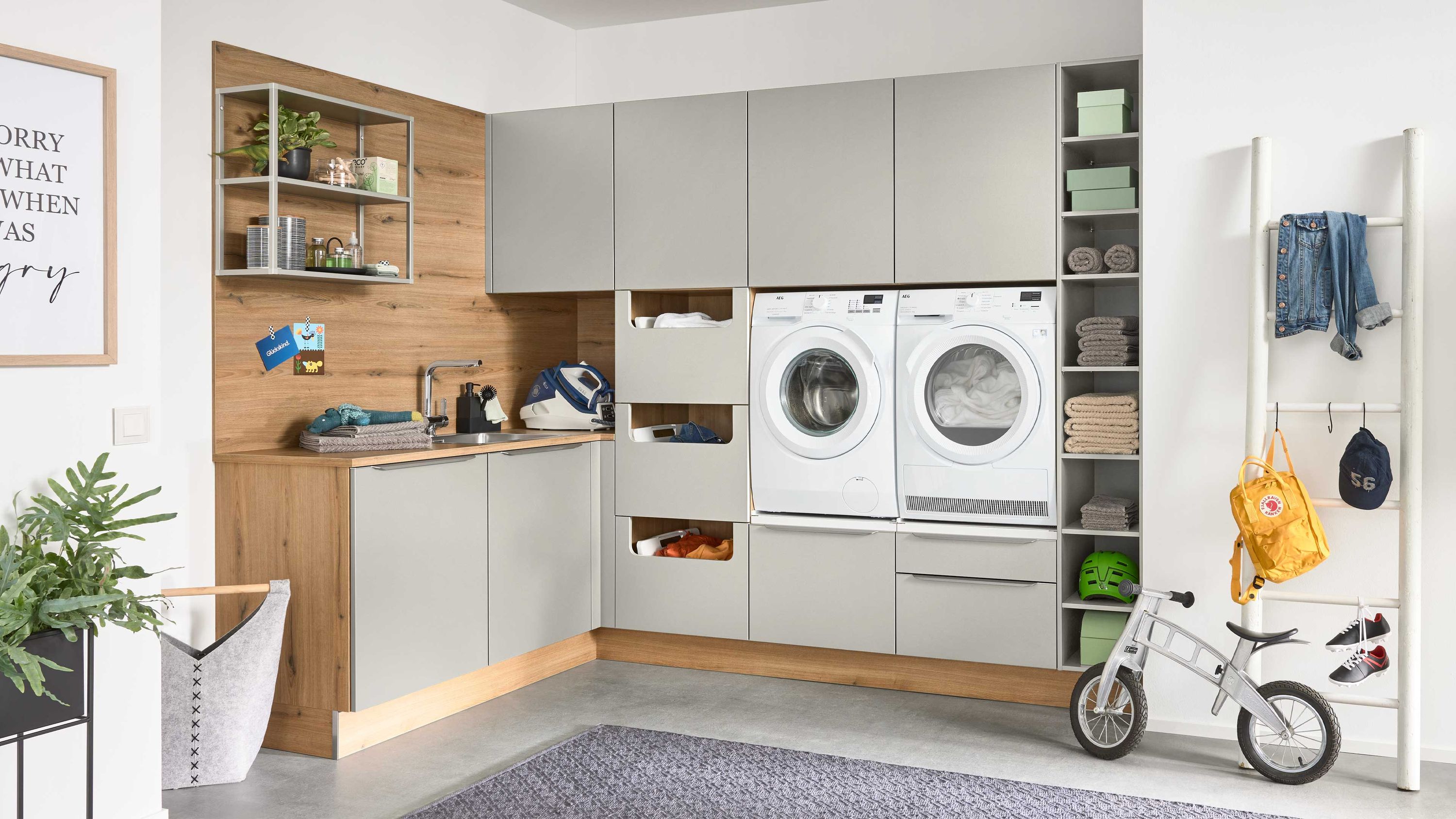 Hauswirtschaftsraum mit Einbauschränken Wasch-Trockner-Turm offenen Regalen Fahrrad Garderobe grauer Teppich