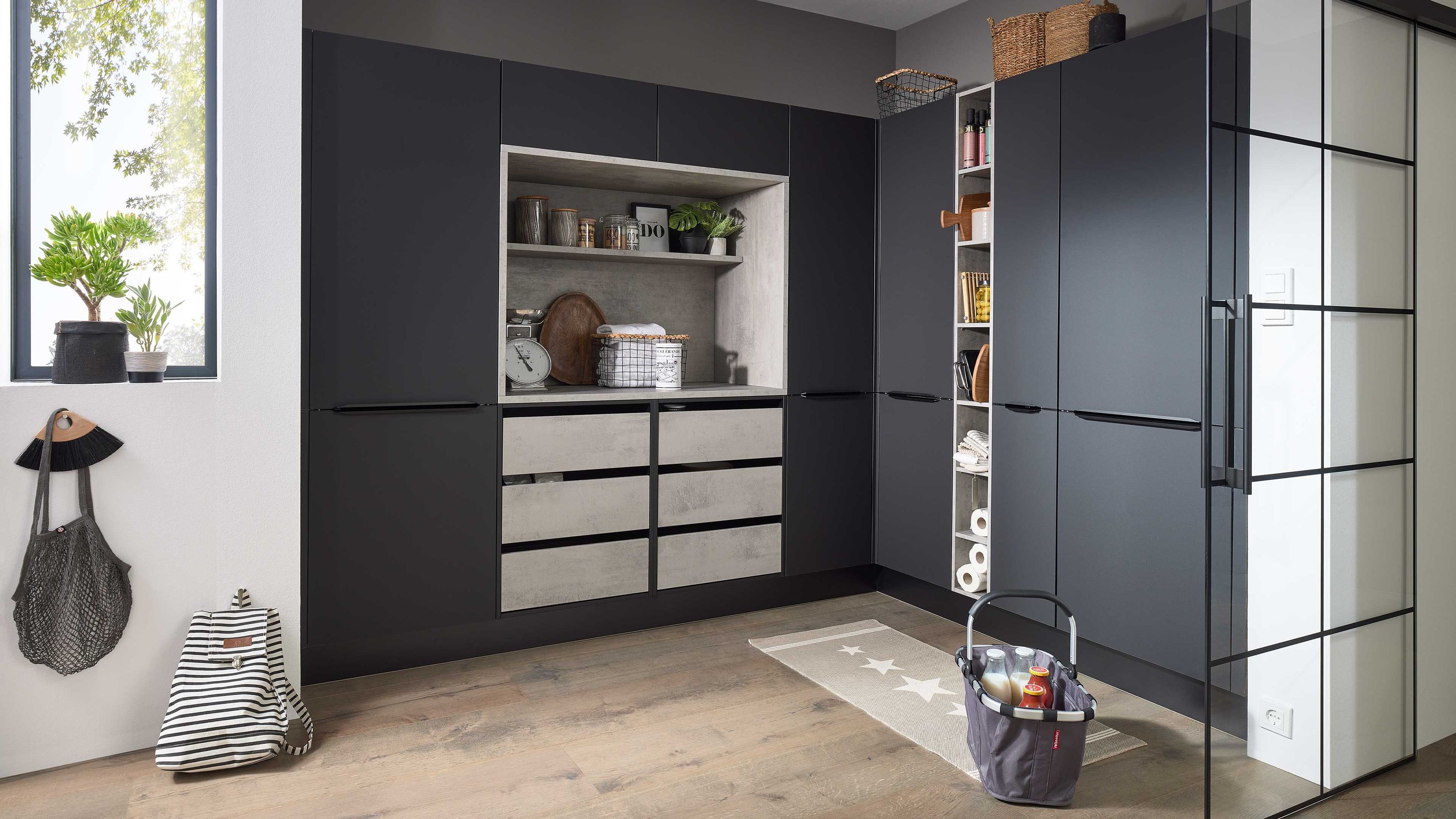 Funktionale Küche mit Kontrastoptik Tageslicht und praktischen Stauraumlösungen Dunkle Küche mit hellen Arbeitsflächen Fensterlicht offenen Regalen grauer Tasche an der Wand Korb mit Putzmitteln