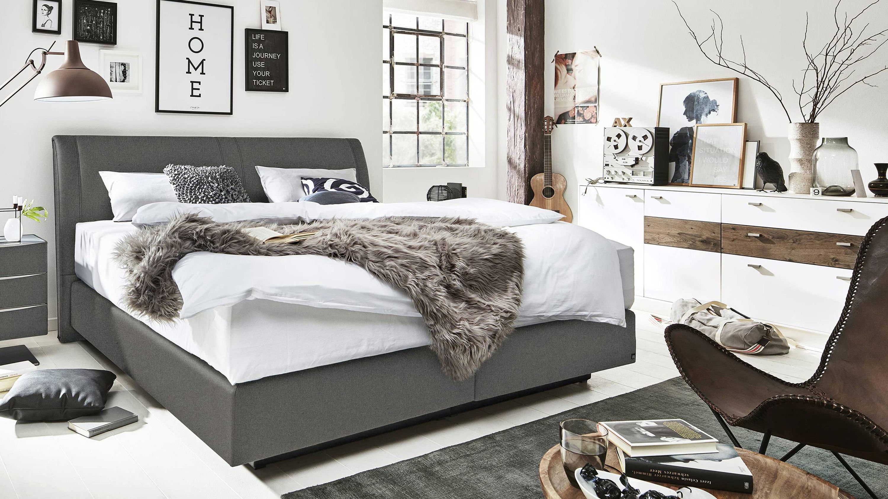 Graues Boxspringbett mit gepolstertem Kopfteil und weißer Bettwäsche in modernem Schlafzimmer