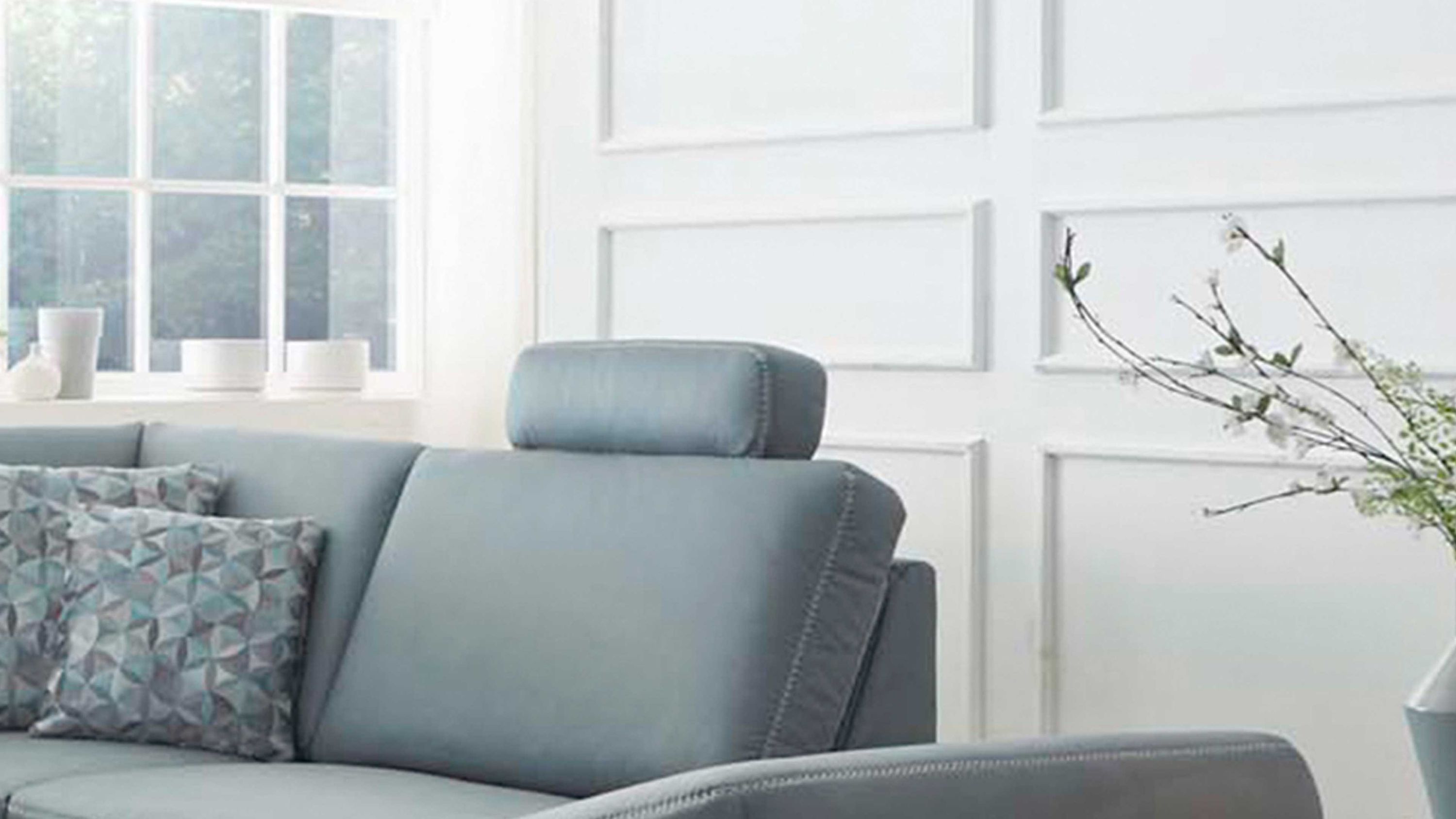 Sitzgruppe mit hellblauem Sofa zwei gemusterten Kissen und stahlfarbener Kopfstütze