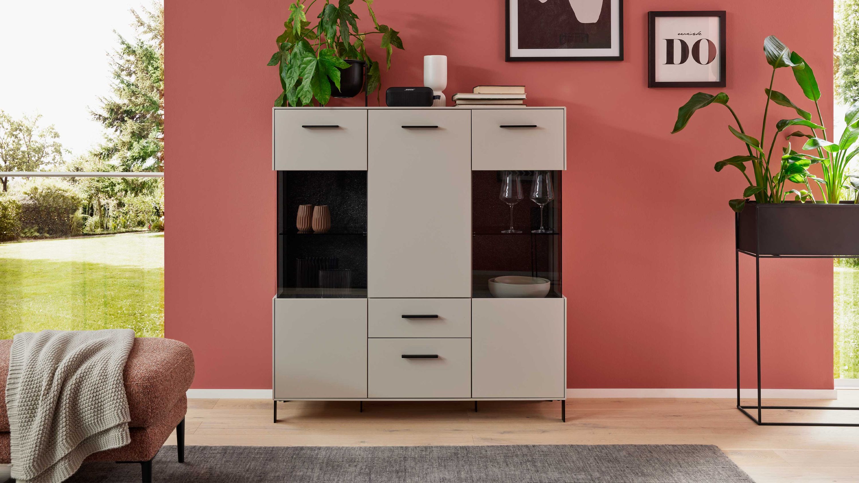 Highboard mit Türen und Schubladen in Creme Helles Highboard mit drei Türen zwei Schubladen und Glasfächern cremefarben vor roter Wand